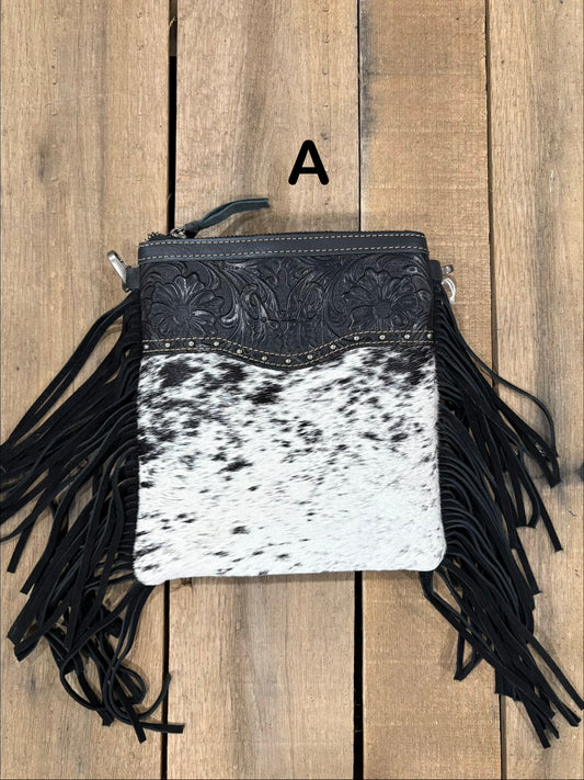 Black and white cowhide leather crossbody bag with fringe on a wooden background