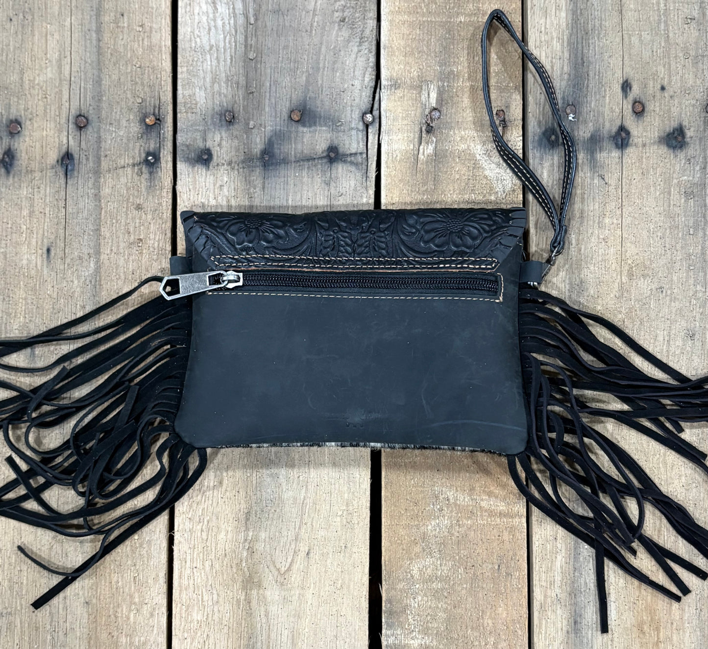 Black leather clutch with fringe on a wooden surface