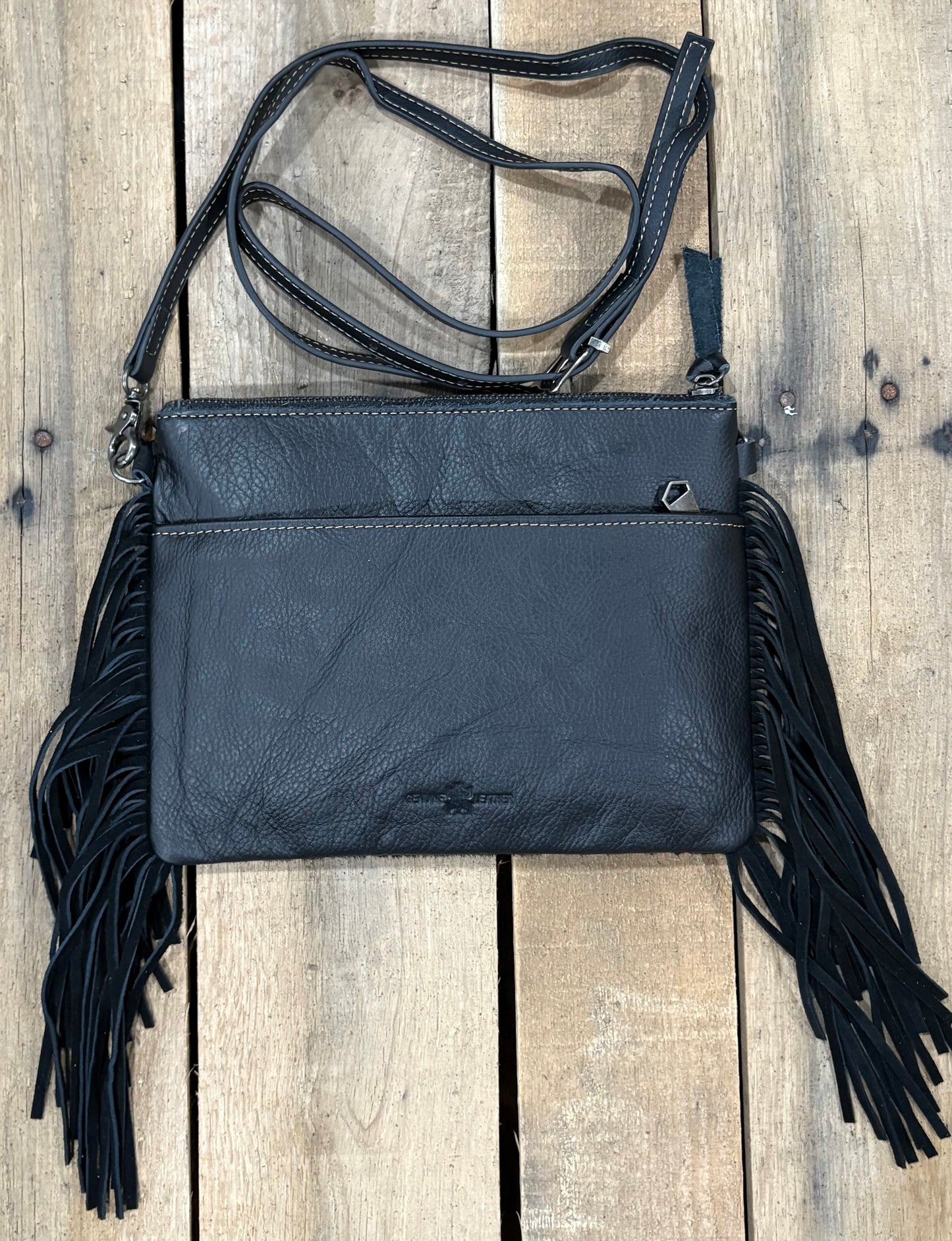 Black leather crossbody bag with fringe on a wooden background