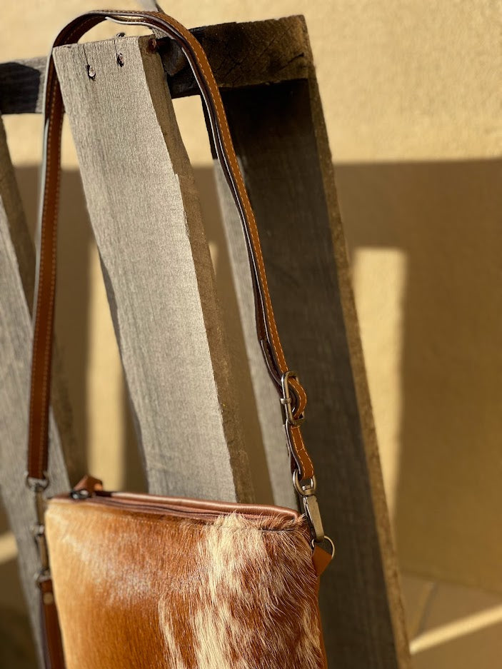 Brown leather handbag with a textured strap on a wooden surface.