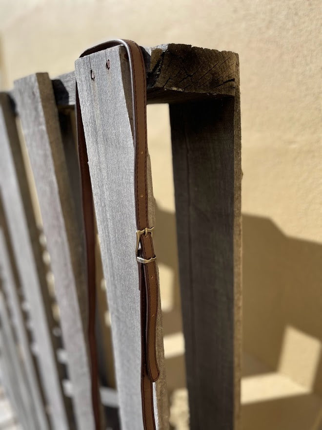 Close-up of a wooden frame with a leather strap against a beige wall.