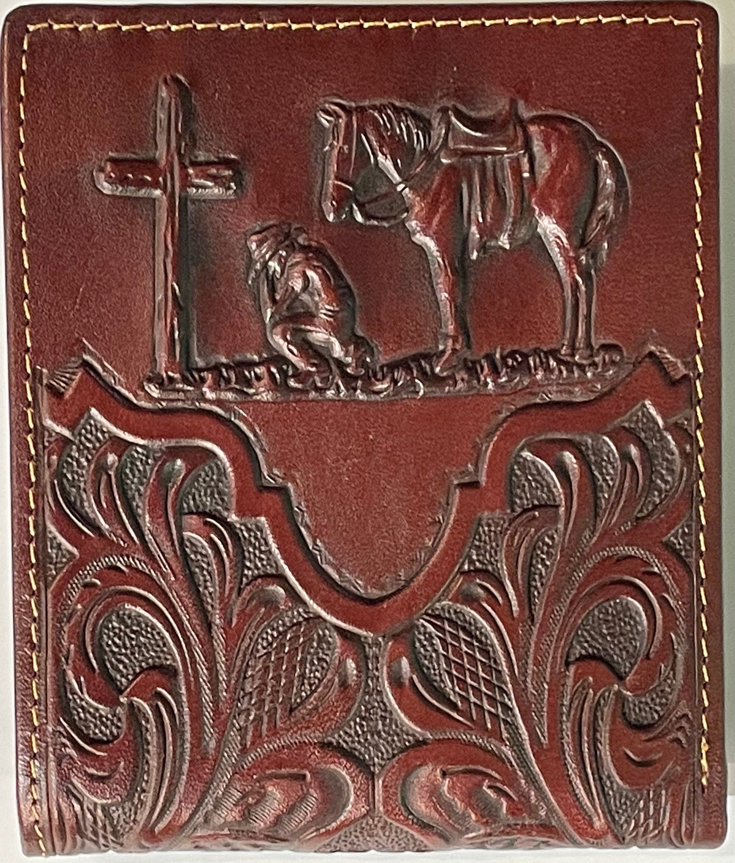 Close up of a Brown leather wallet with embossed designs of a cross, horse, and bird on a gray background