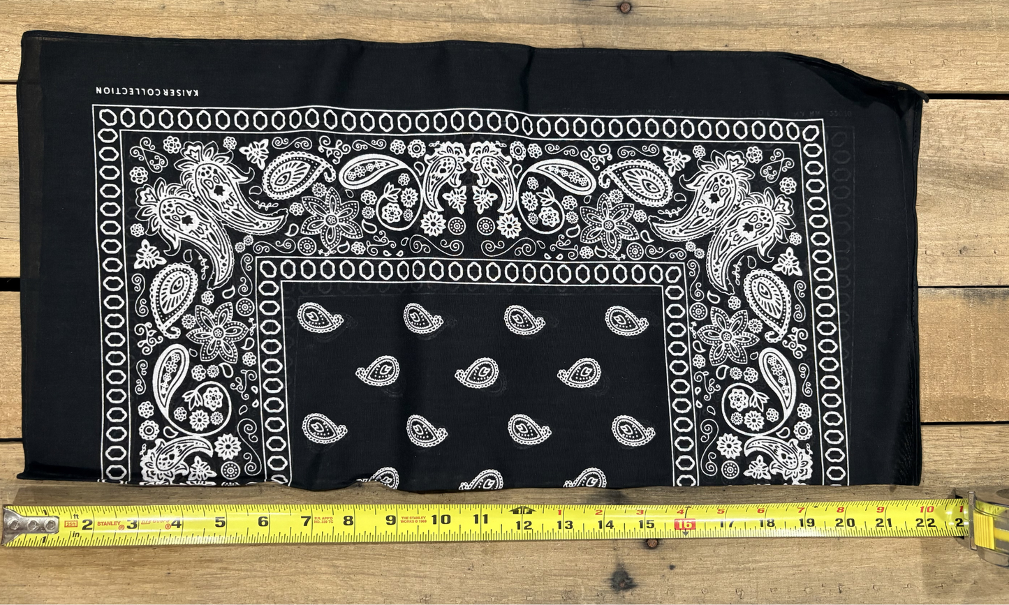 Black bandana with white paisley patterns on a wooden surface, measured by a yellow tape measure.