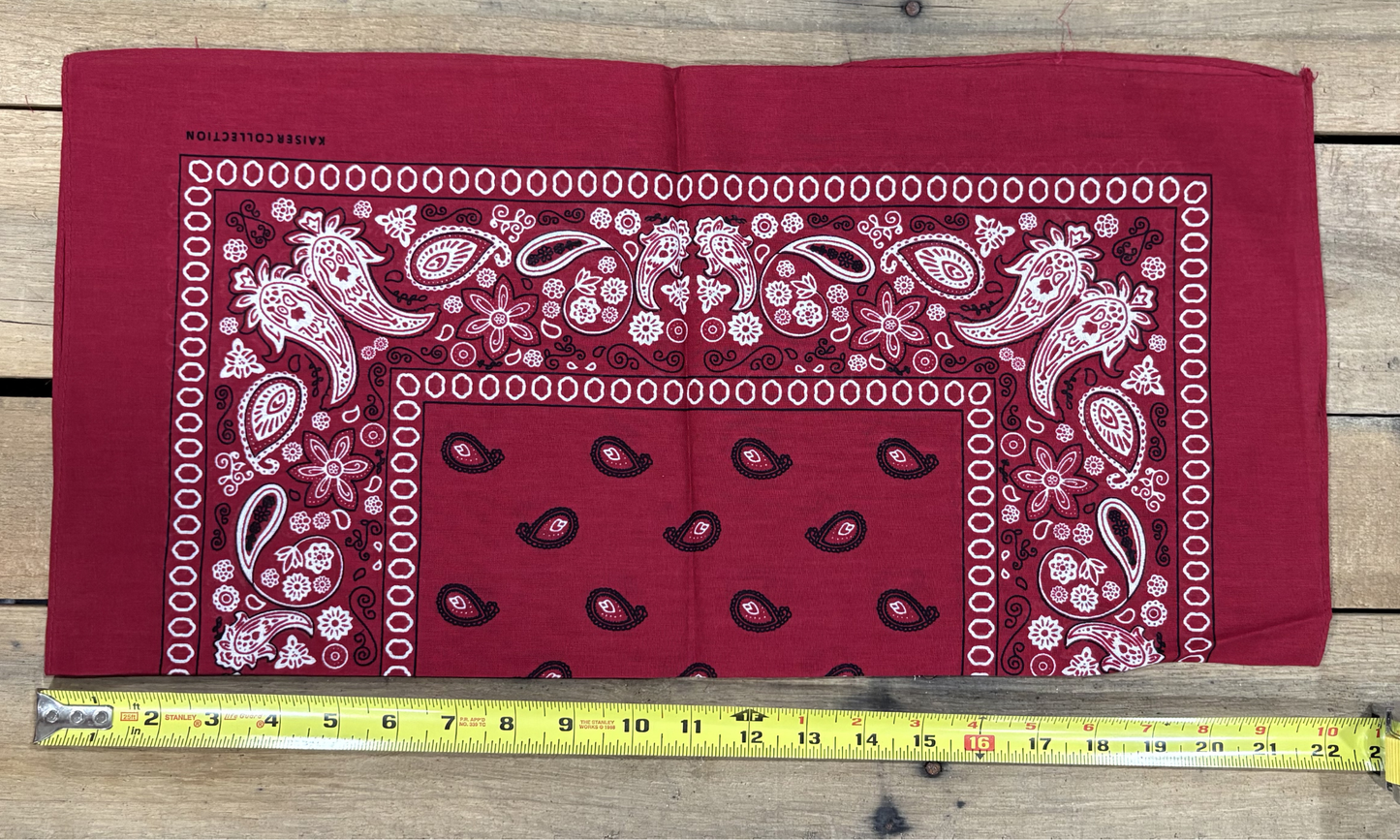 Burgundy bandana with white paisley patterns on a wooden surface, measured by a yellow tape measure.