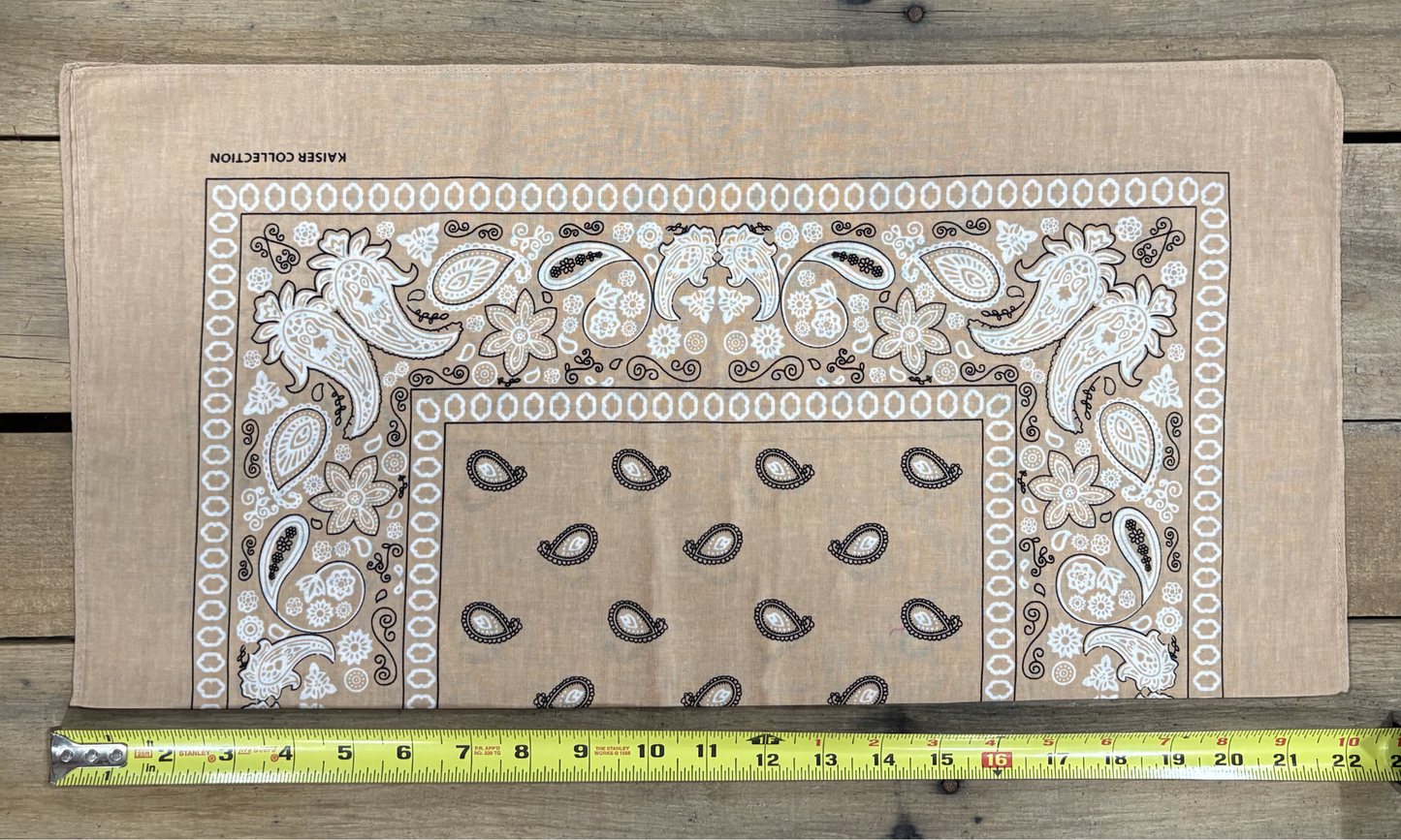 Khaki bandana with white paisley patterns on a wooden surface, measured by a yellow tape measure.