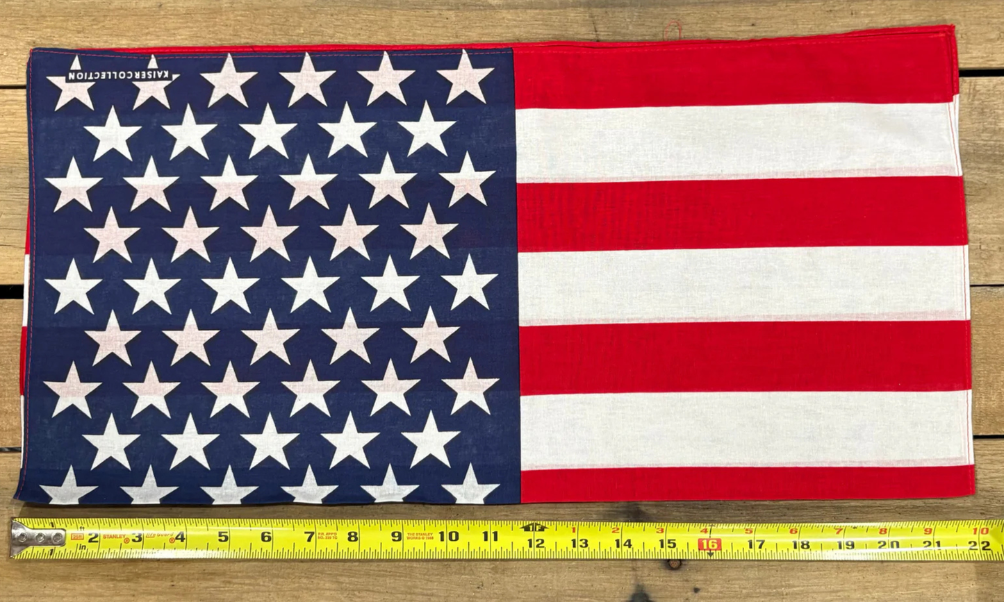 American Flag bandana with white paisley patterns on a wooden surface, measured by a yellow tape measure.