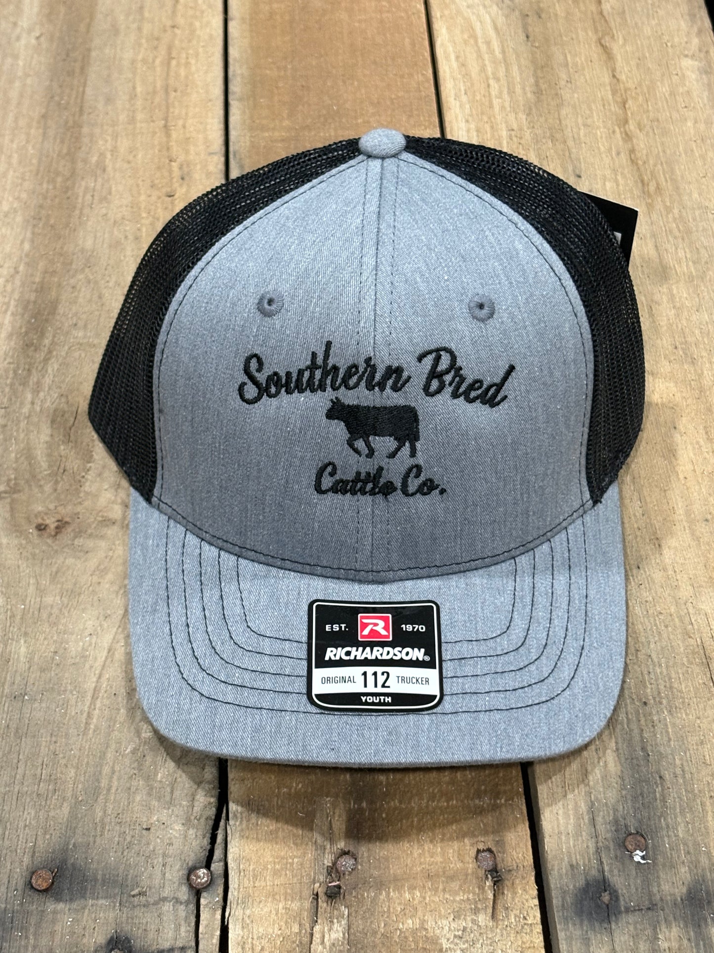 Gray and black cap with 'Southern Bred Cattle Co.' logo on a wooden surface