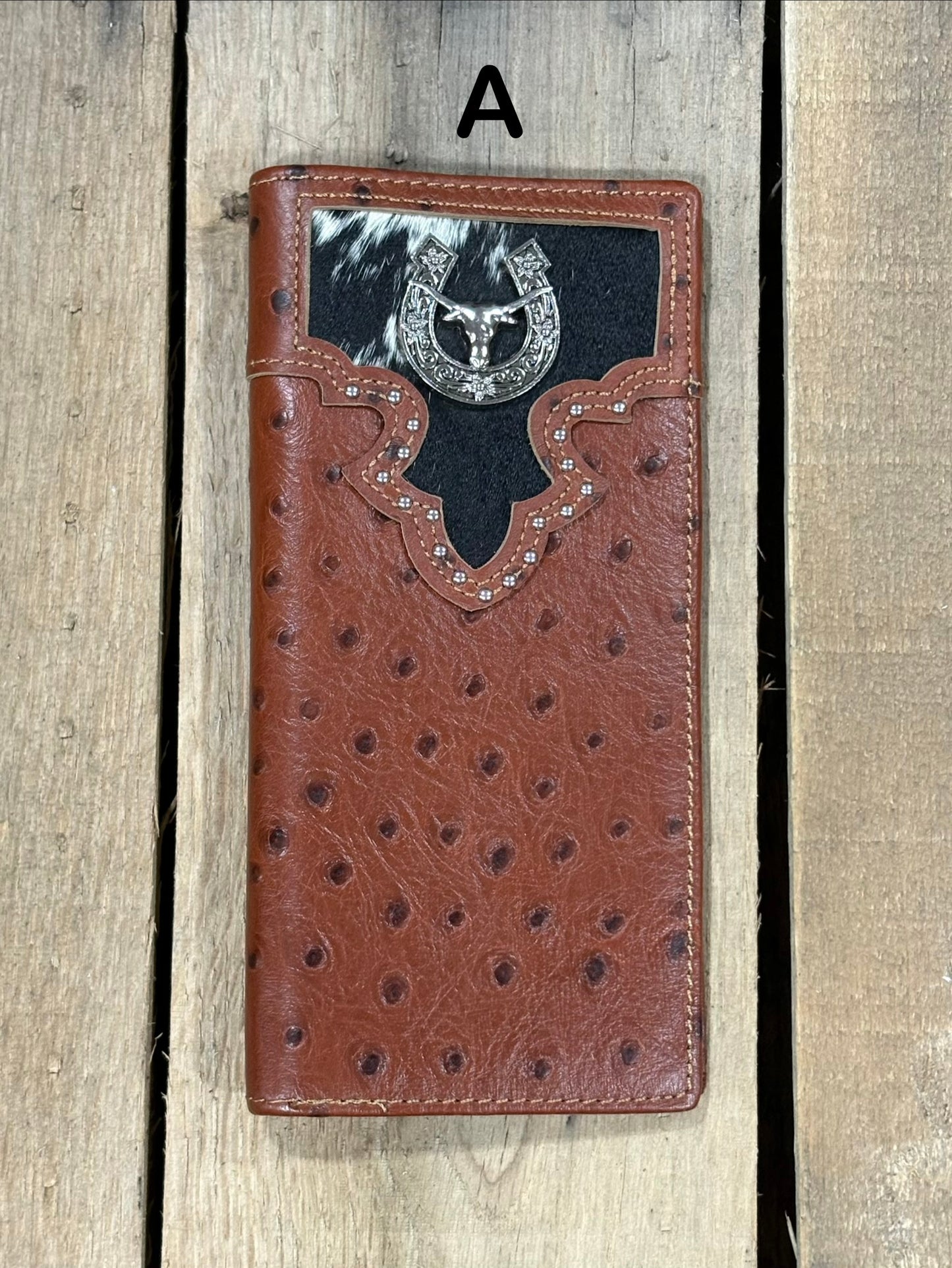 Brown leather wallet with cowhide pattern and horseshoe and longhorn concho on a wooden surface