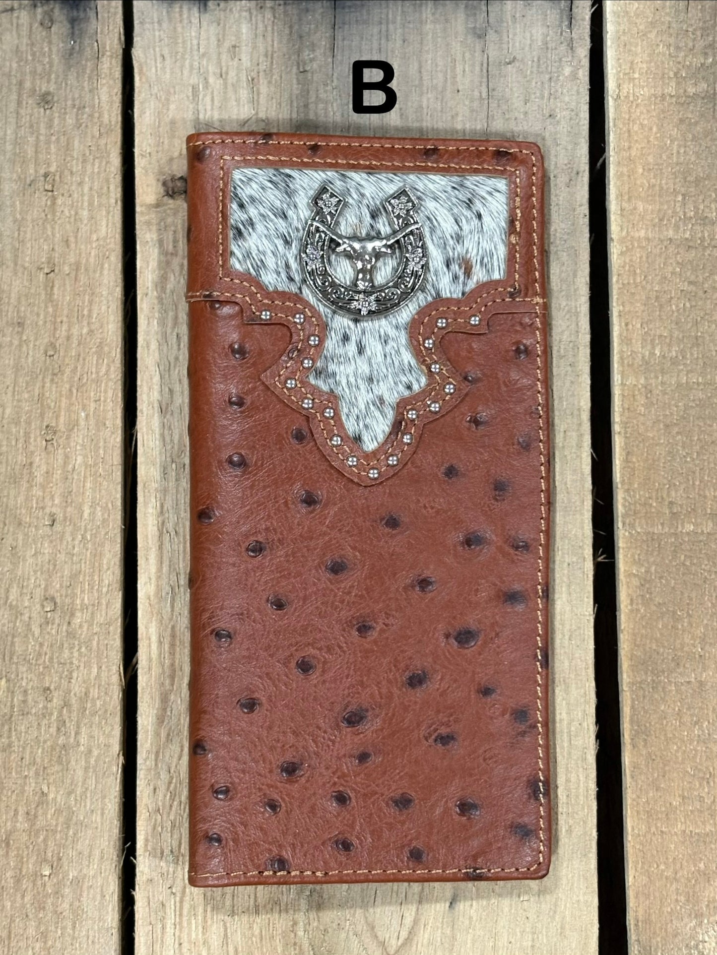 Brown leather wallet with cowhide pattern and horseshoe and longhorn concho on a wooden surface