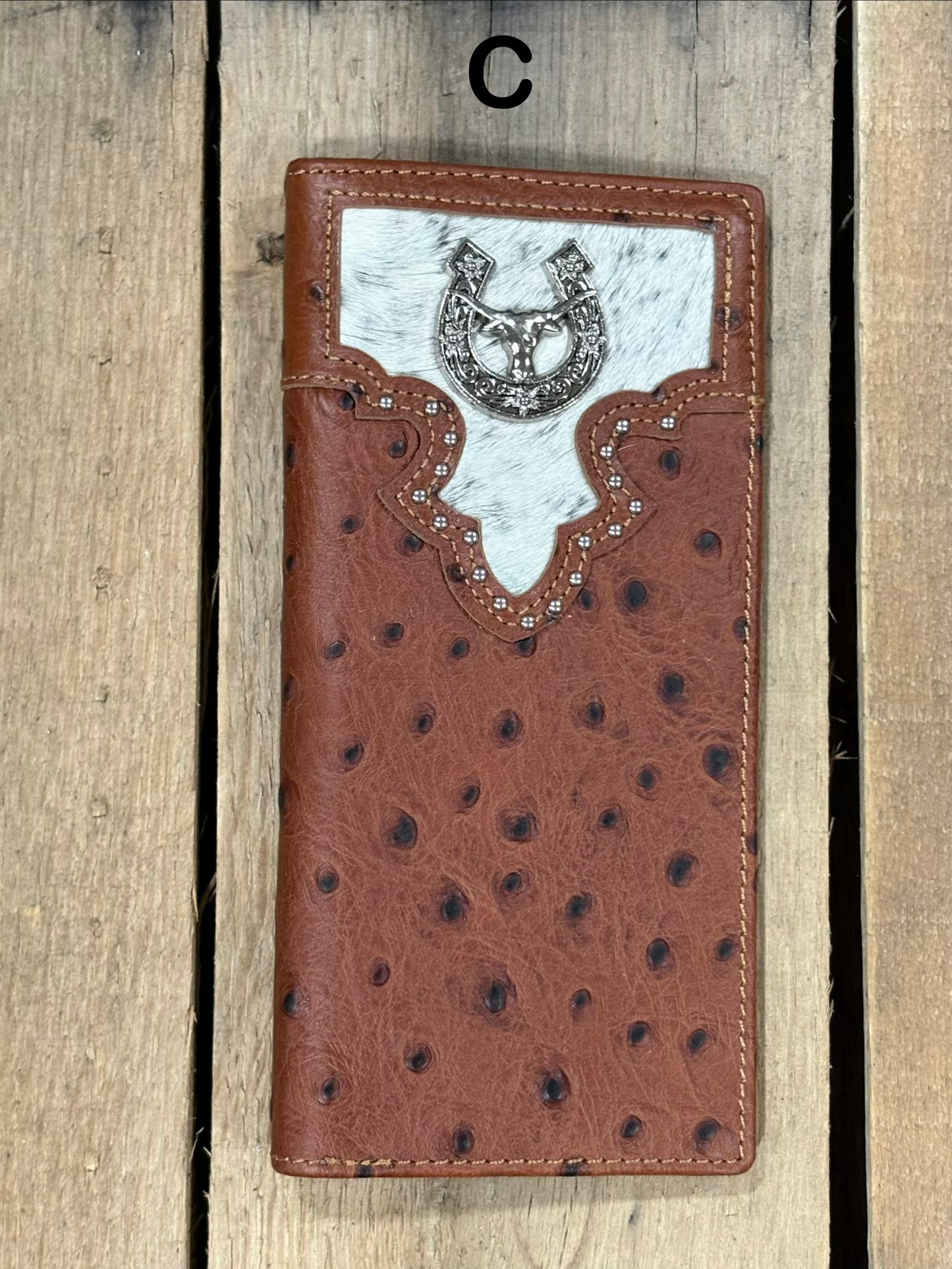 Brown leather wallet with cowhide pattern and horseshoe and longhorn concho on a wooden surface