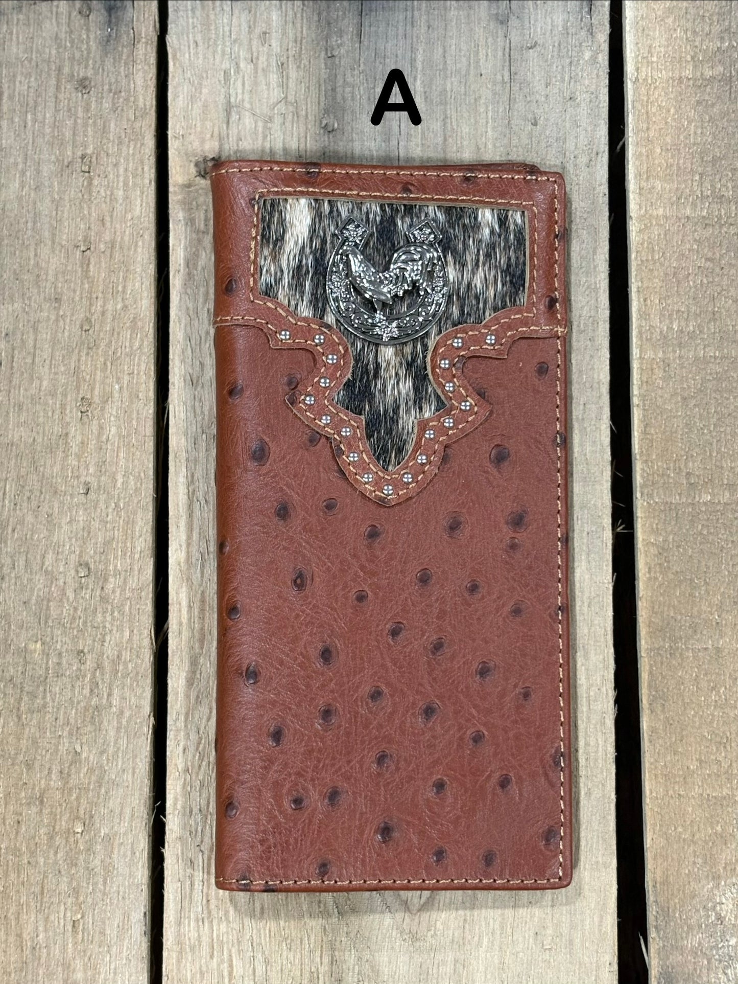 Brown leather wallet with cowhide pattern and horseshoe and rooster concho on a wooden surface