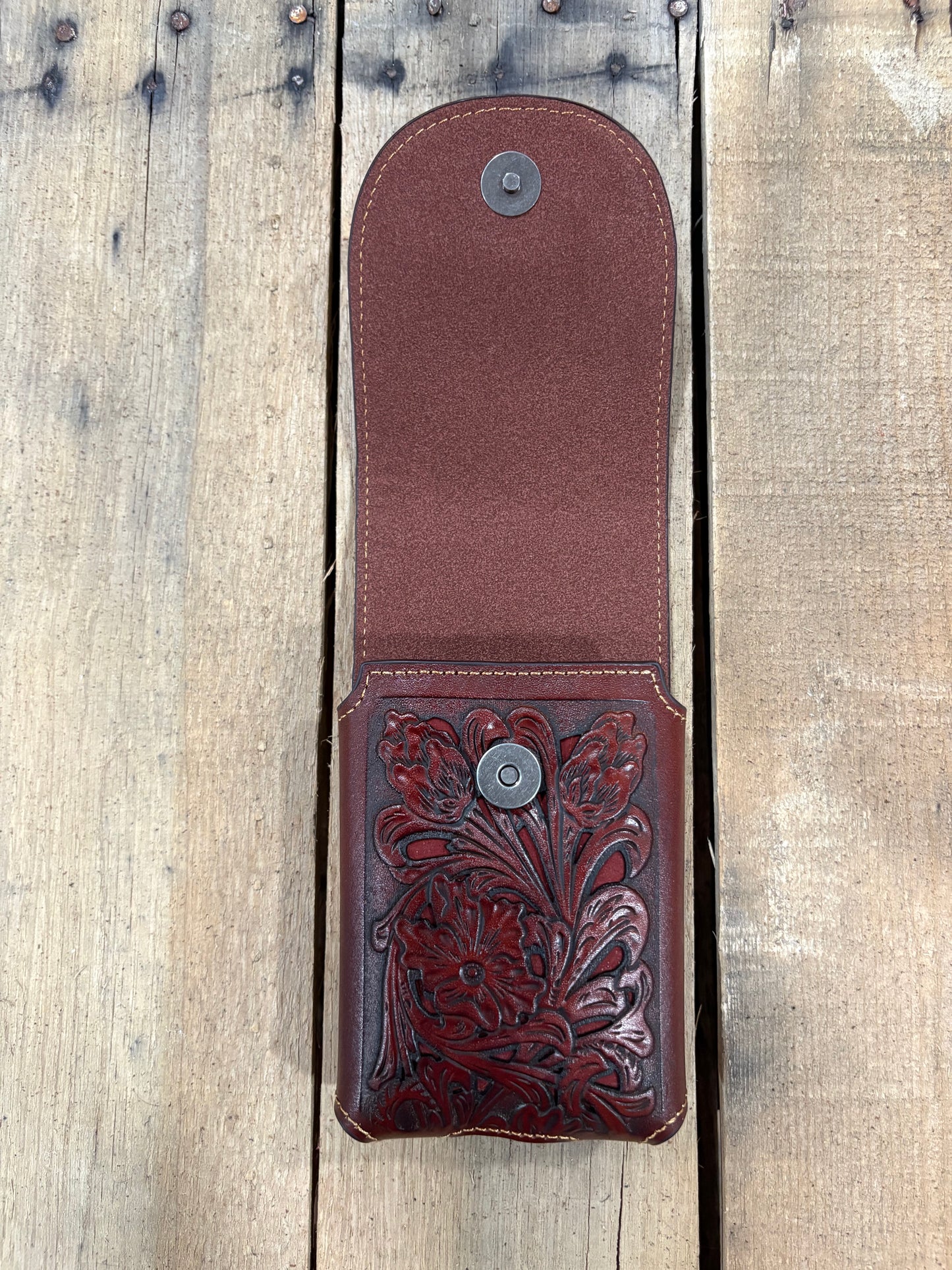 Brown leather case with intricate floral embossing on a wooden surface