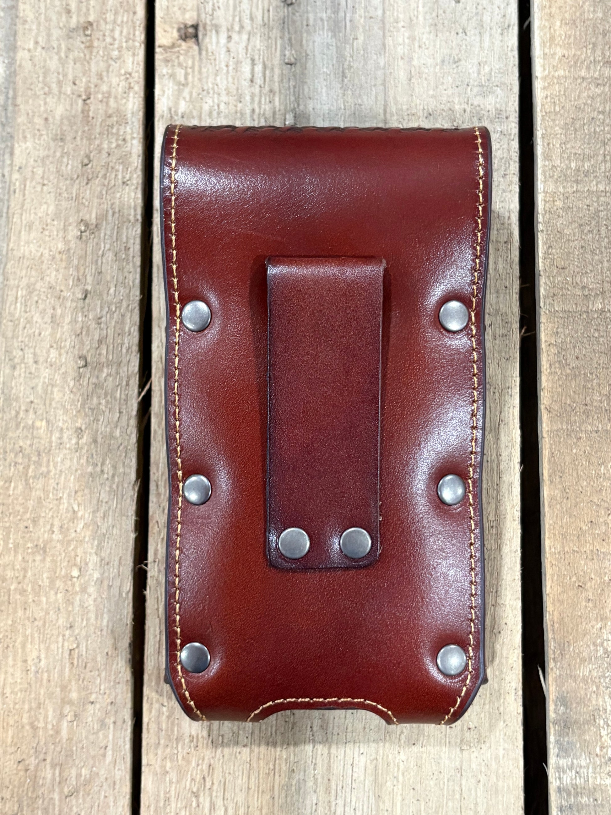 Brown leather phone case with leather belt loop strap on a wooden surface