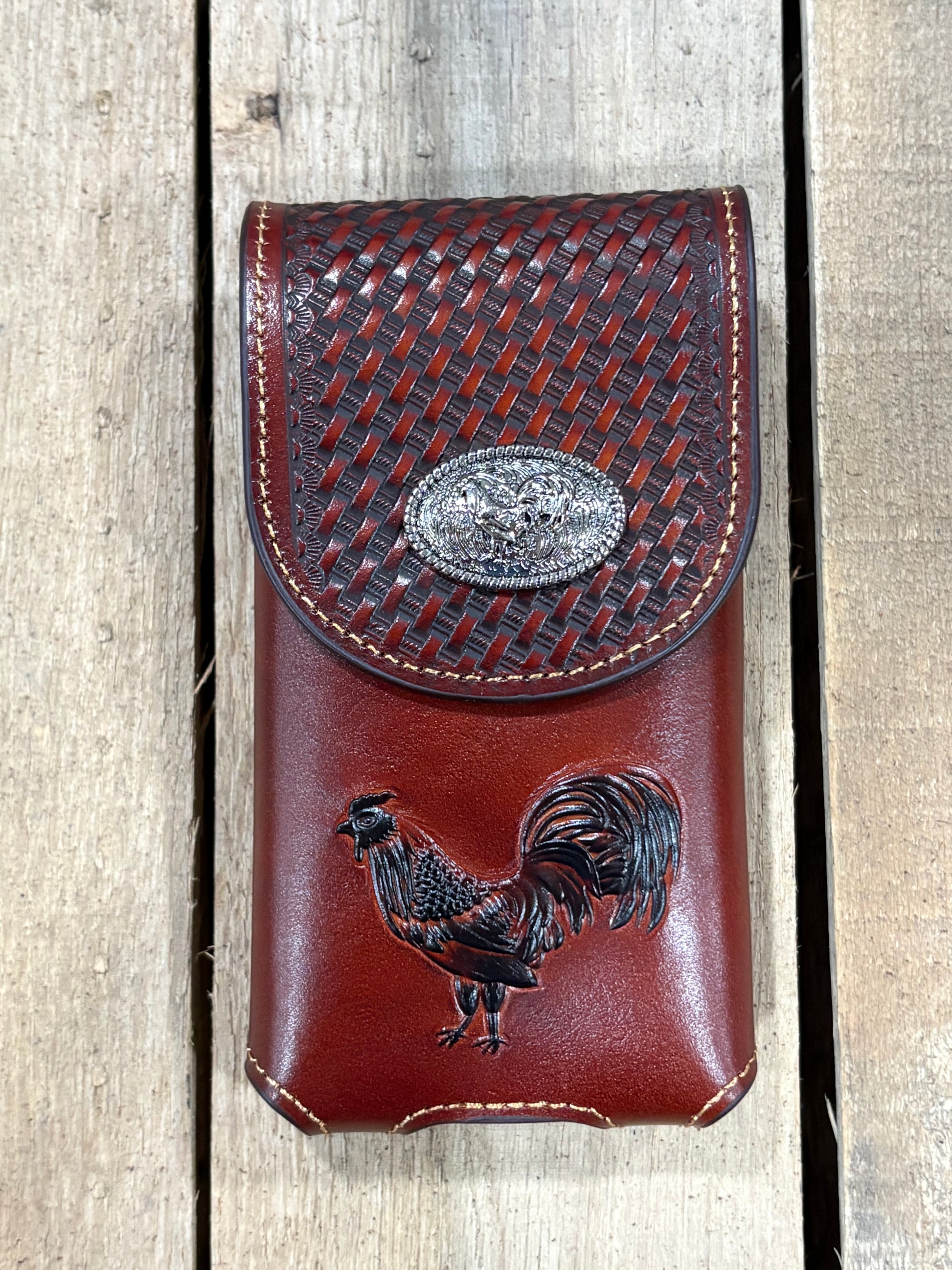 Brown leather phone case with woven top and rooster design on a wooden surface
