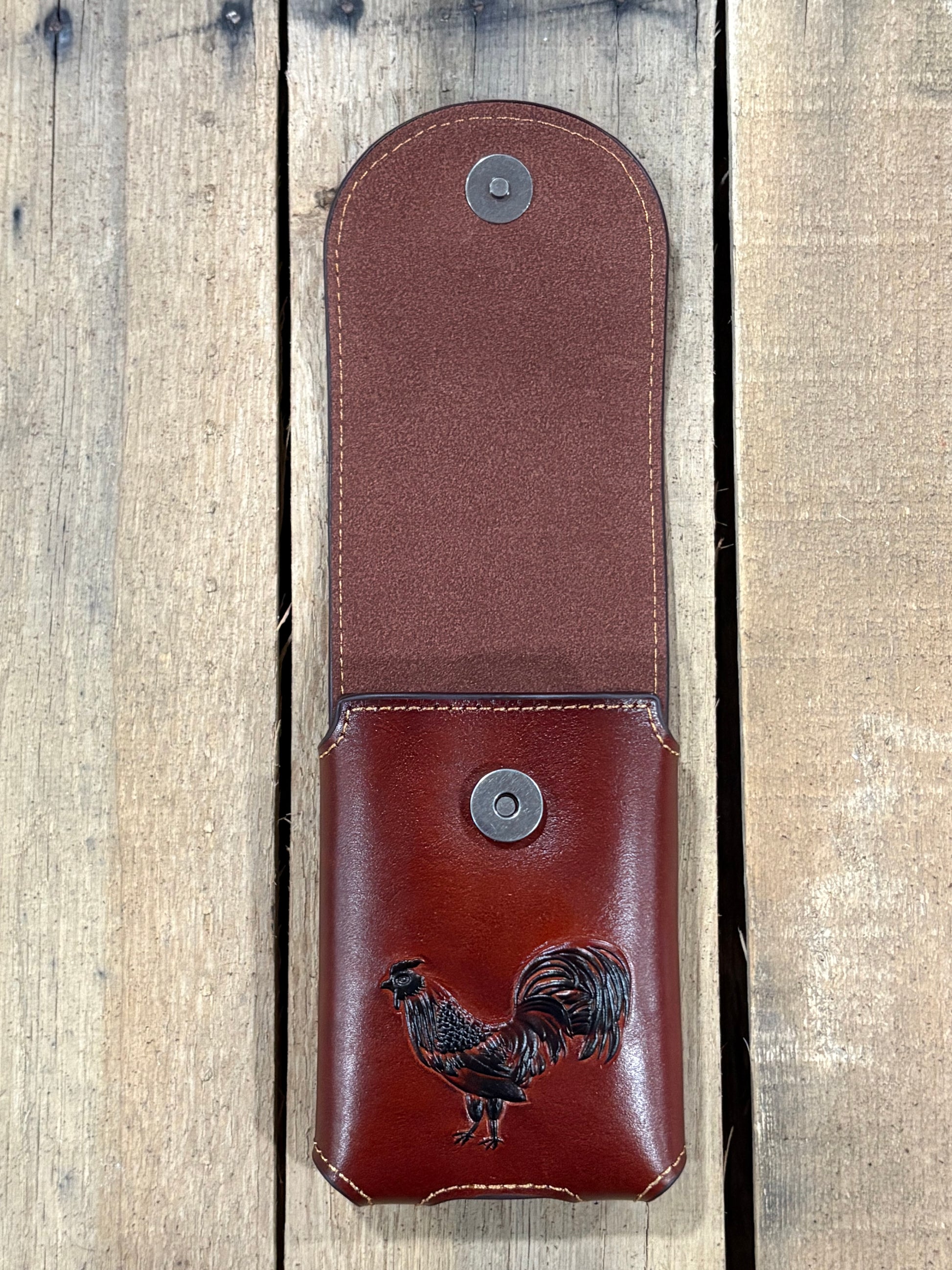 Brown leather case with rooster design on a wooden surface