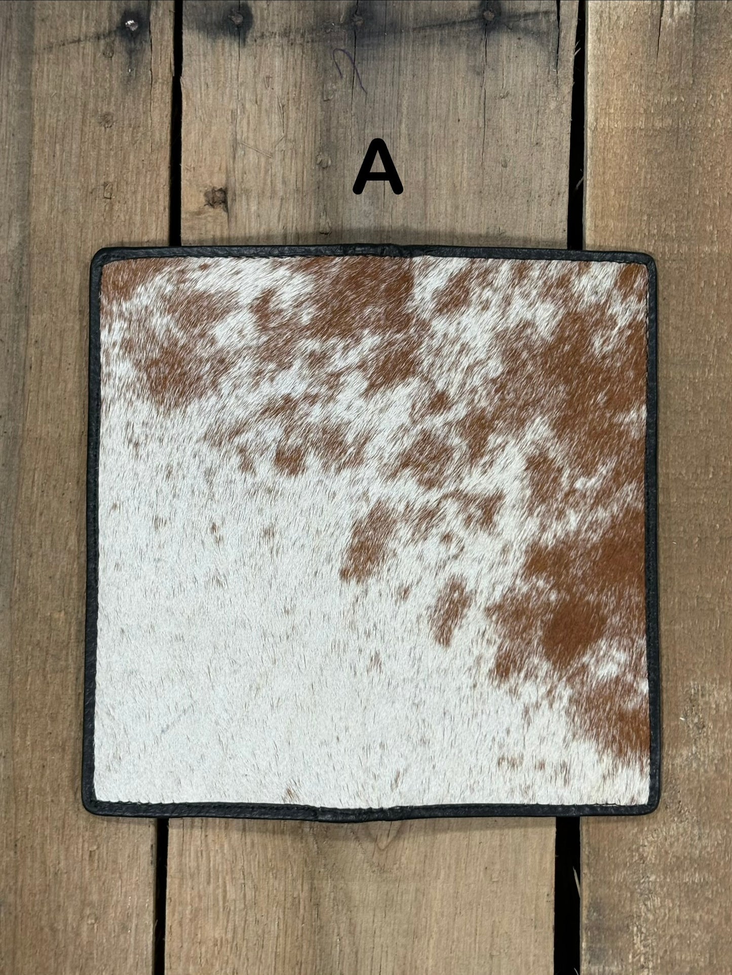 Square piece of cowhide on a wallet with brown and white pattern on a wooden surface