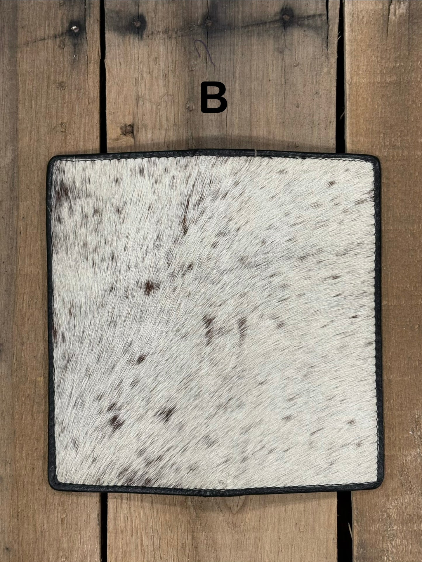 Square piece of cowhide on a wallet with black and white pattern on a wooden surface
