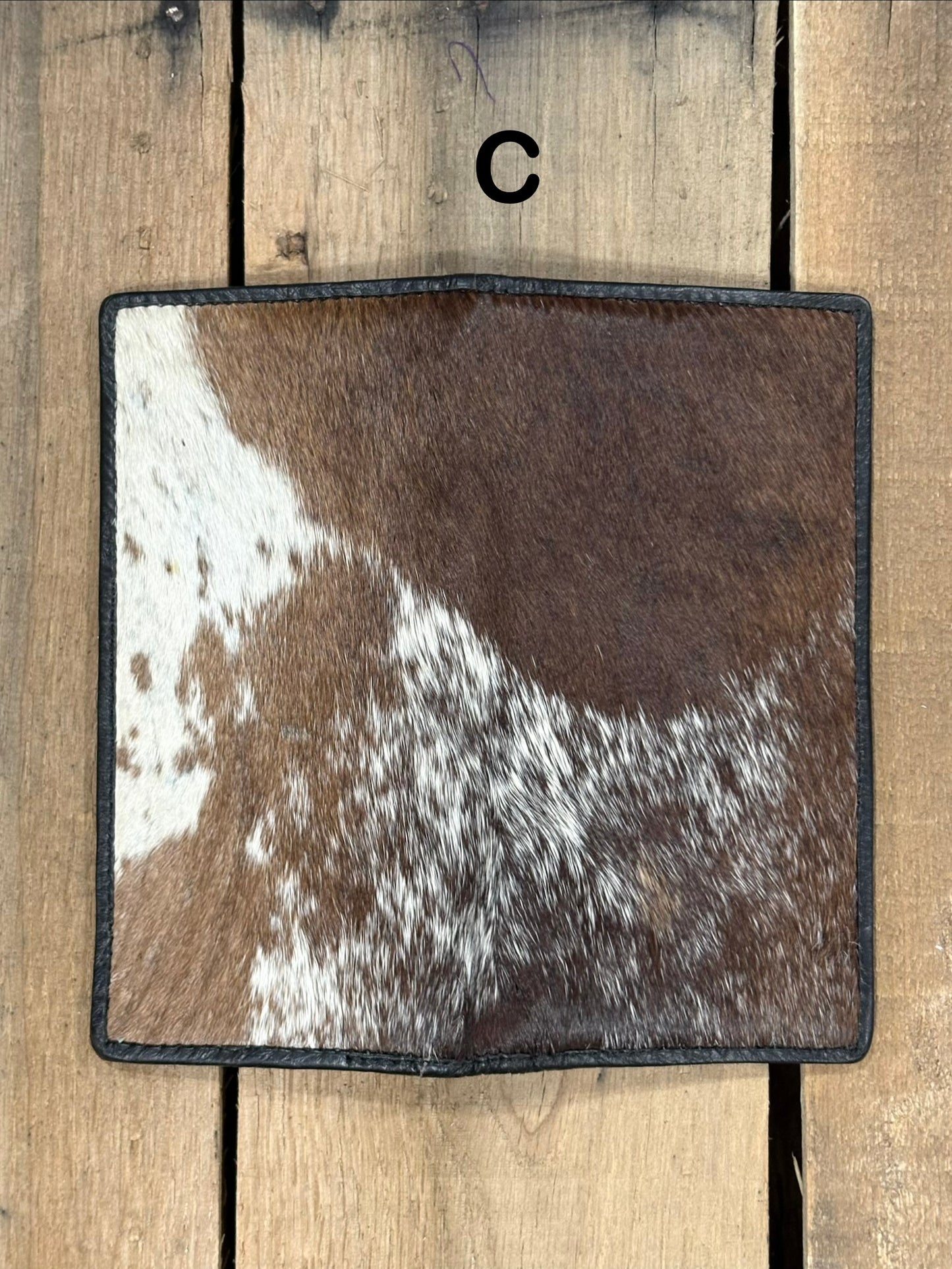 Square piece of cowhide on a wallet with brown and white pattern on a wooden surface