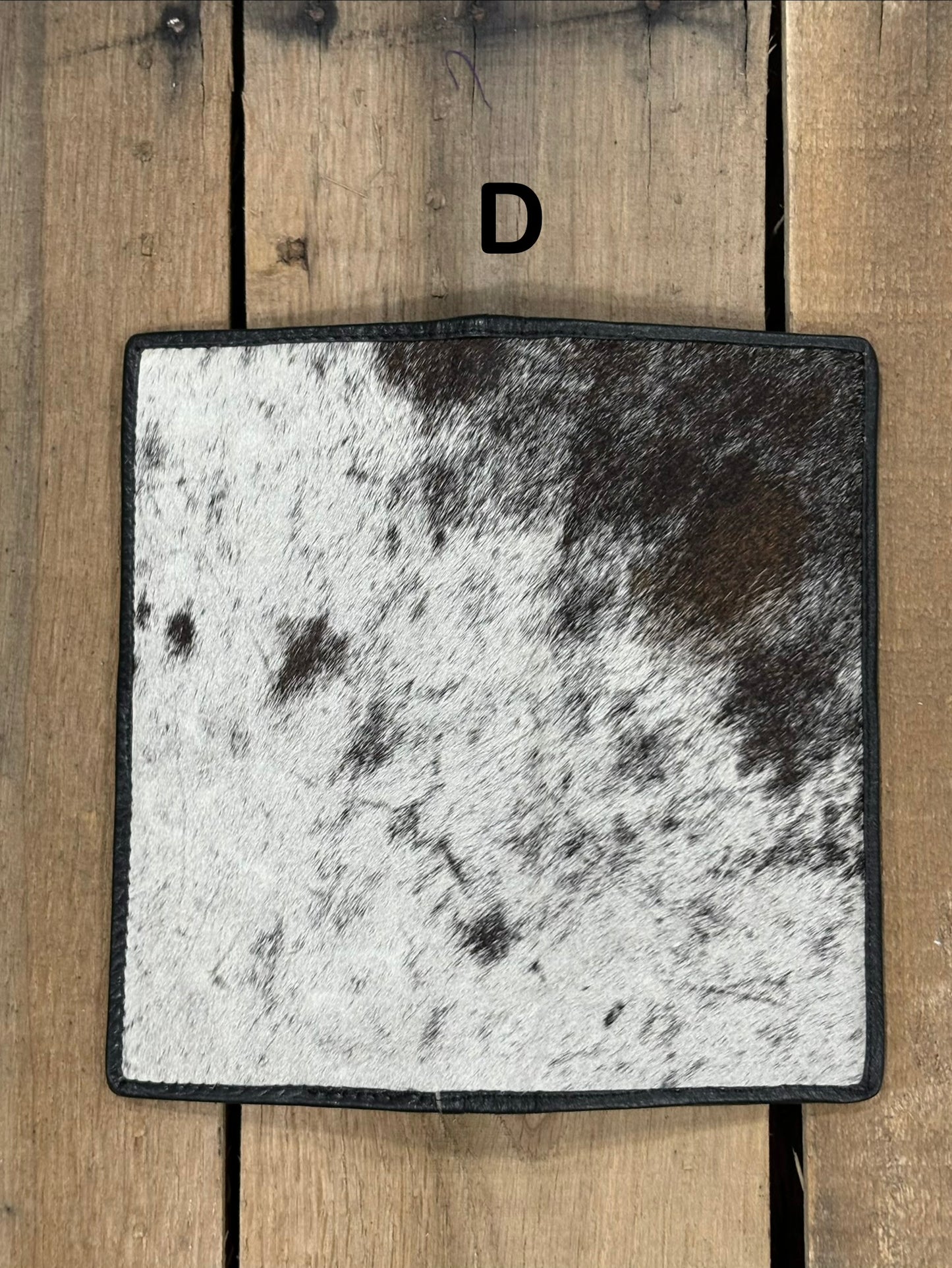 Square piece of cowhide on a wallet with black and white pattern on a wooden surface