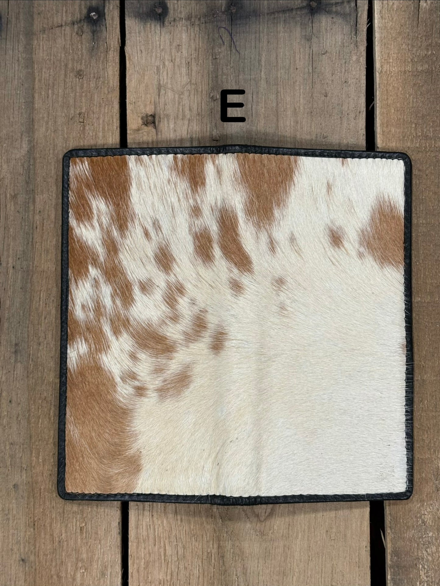 Square piece of cowhide on a wallet with brown and white pattern on a wooden surface