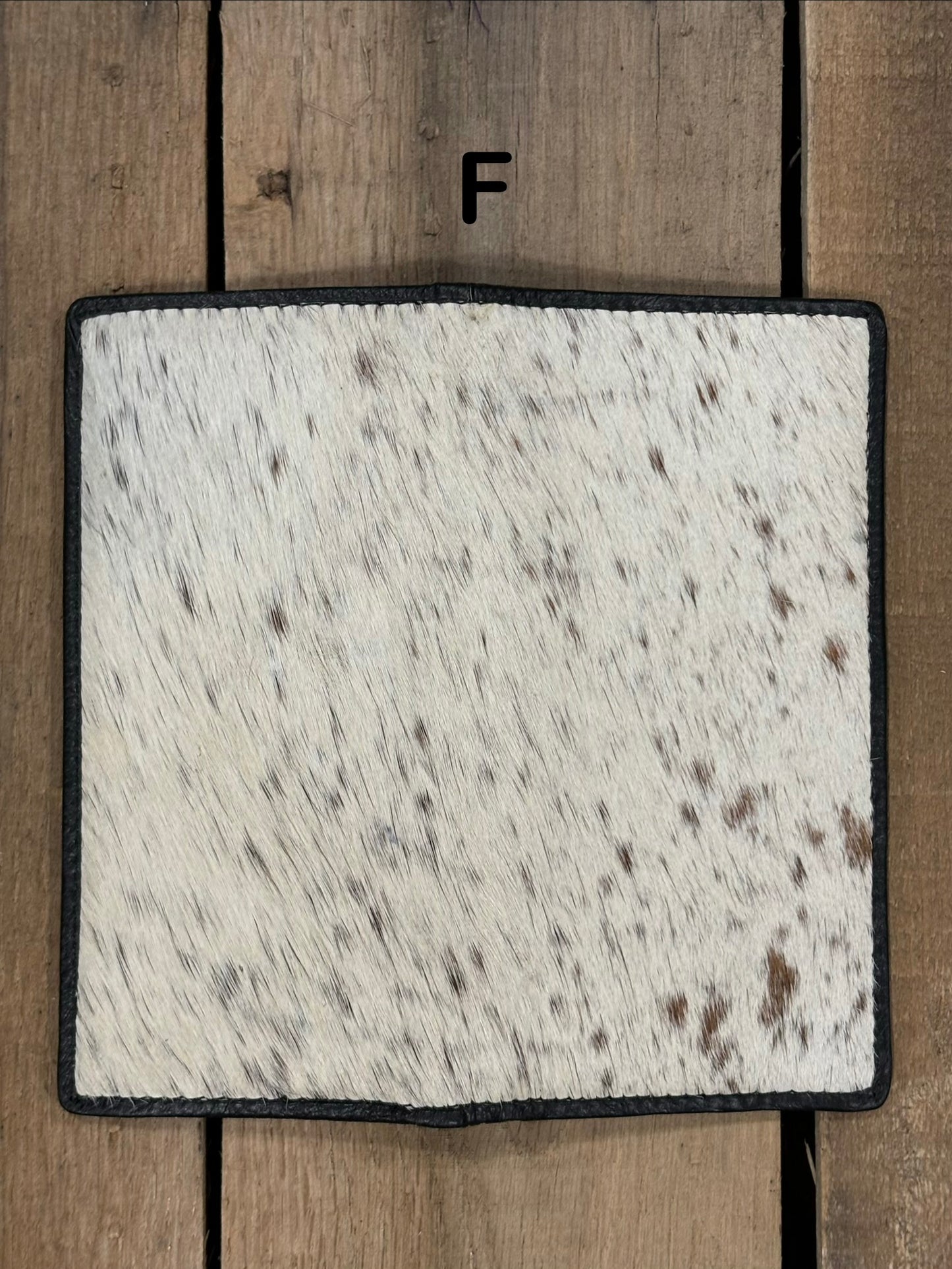 Square piece of cowhide on a wallet with black and white pattern on a wooden surface