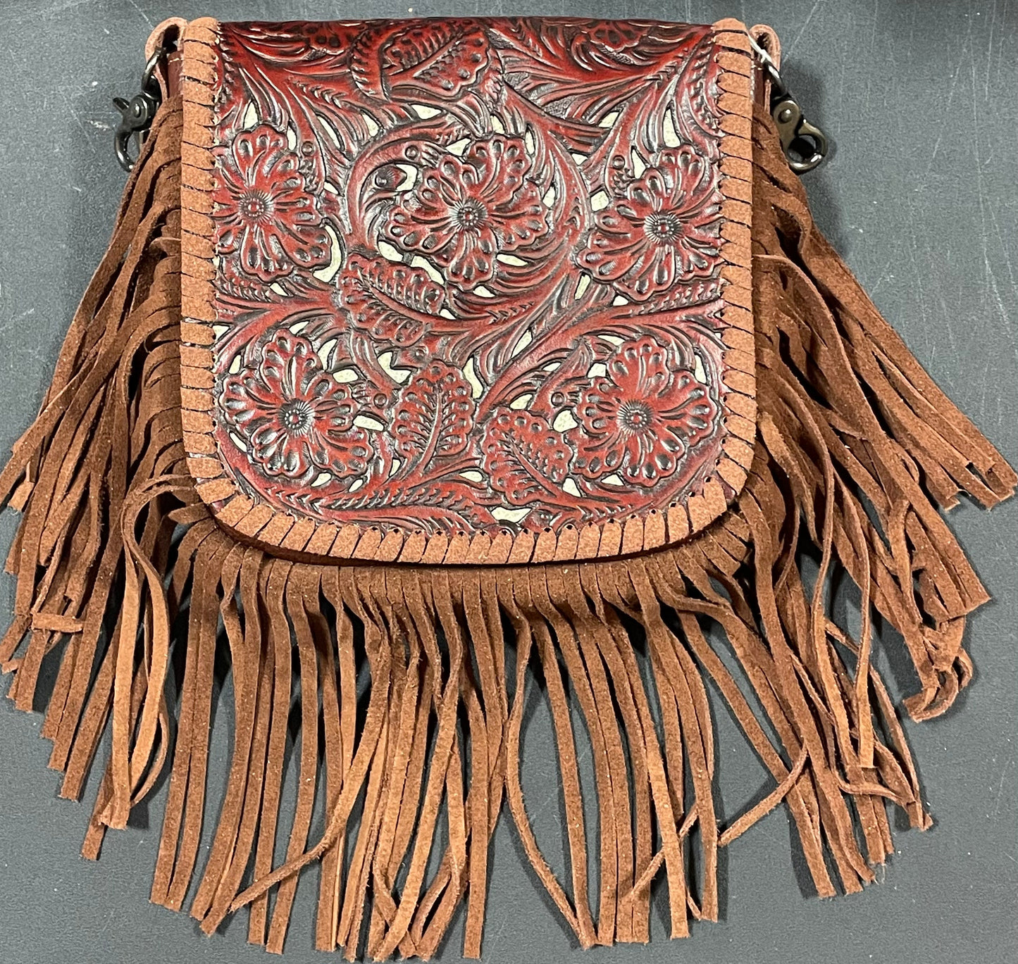 Brown leather handbag with intricate patterns and fringes on a gray background