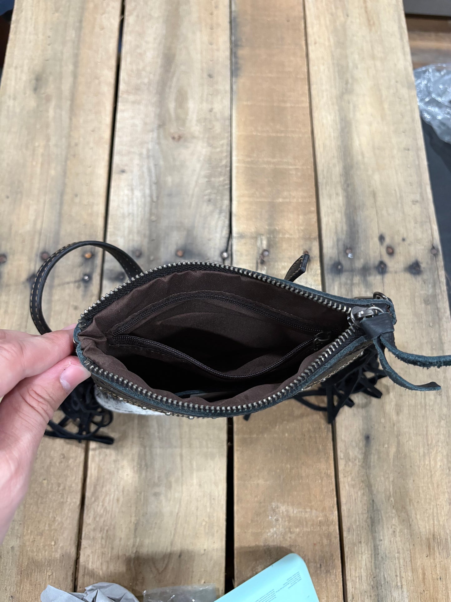 Inside zipper view on a Black leather purse with fringe on a wooden surface