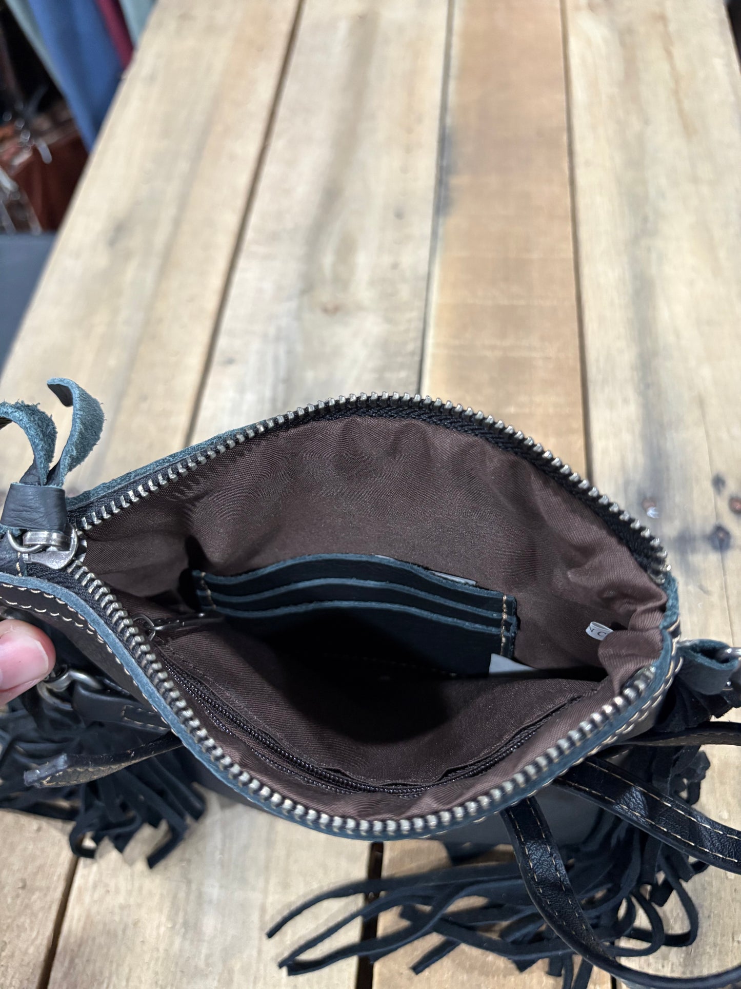 Inside card slot view on a Black leather purse with fringe on a wooden surface