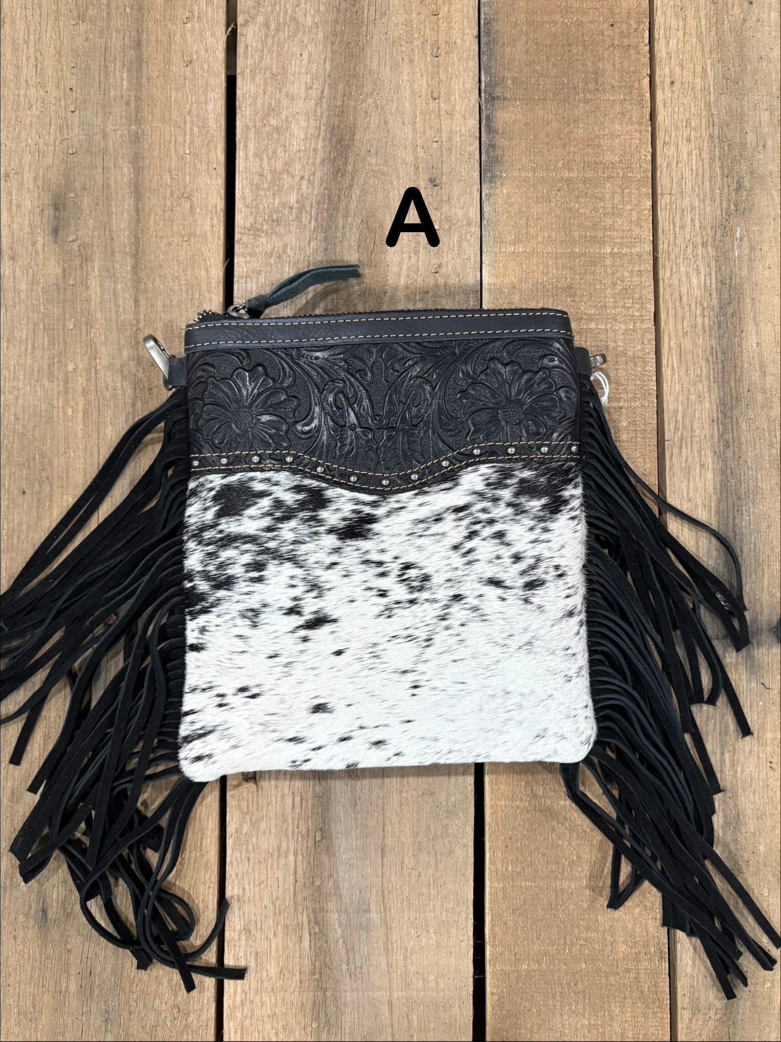 Black and white cowhide leather crossbody bag with fringe on a wooden background