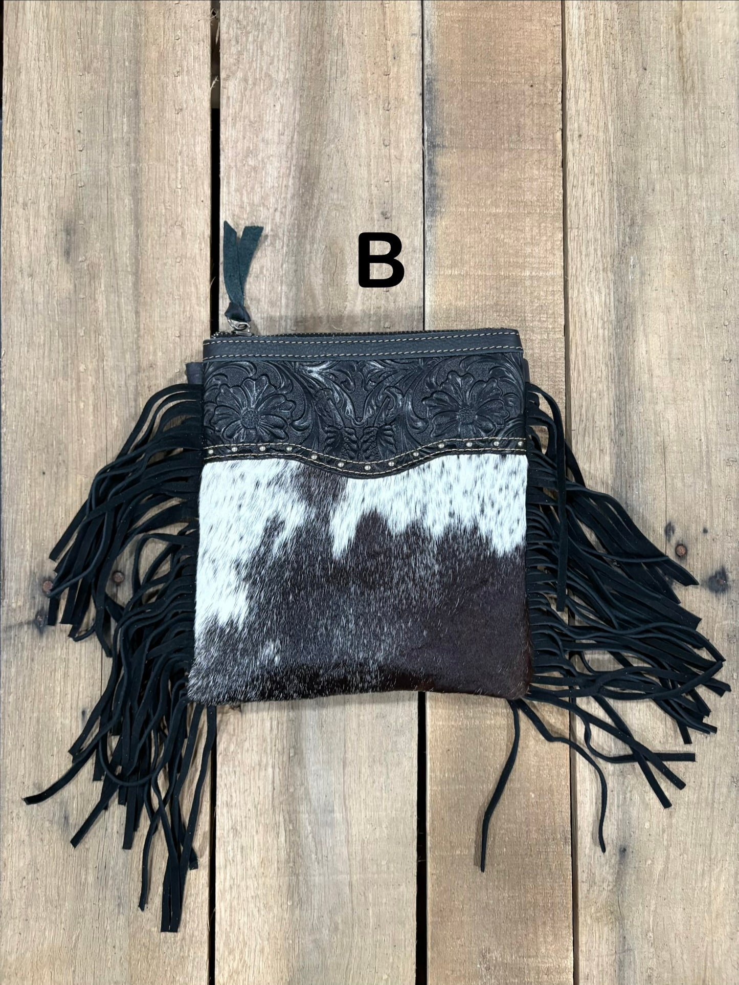 Black and white cowhide handbag with fringe on a wooden surface