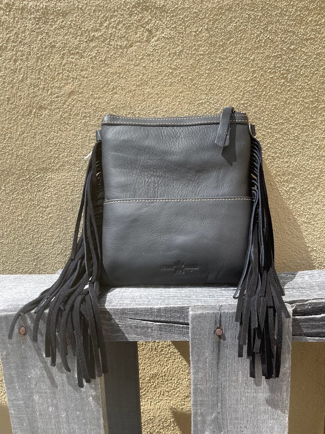 Black leather handbag with fringes on a wooden surface against a beige wall