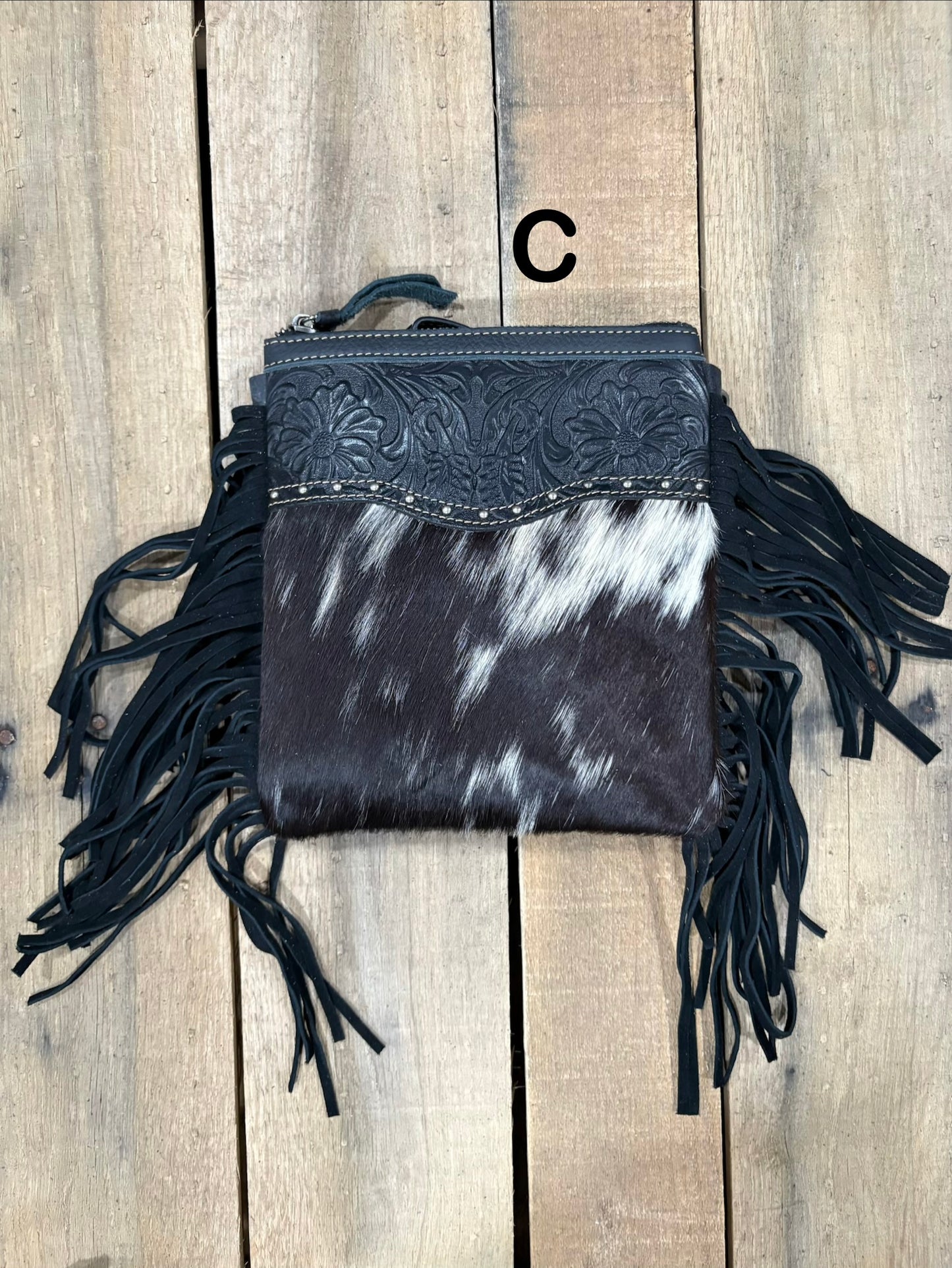 Black and white cowhide leather bag with fringe on a wooden surface