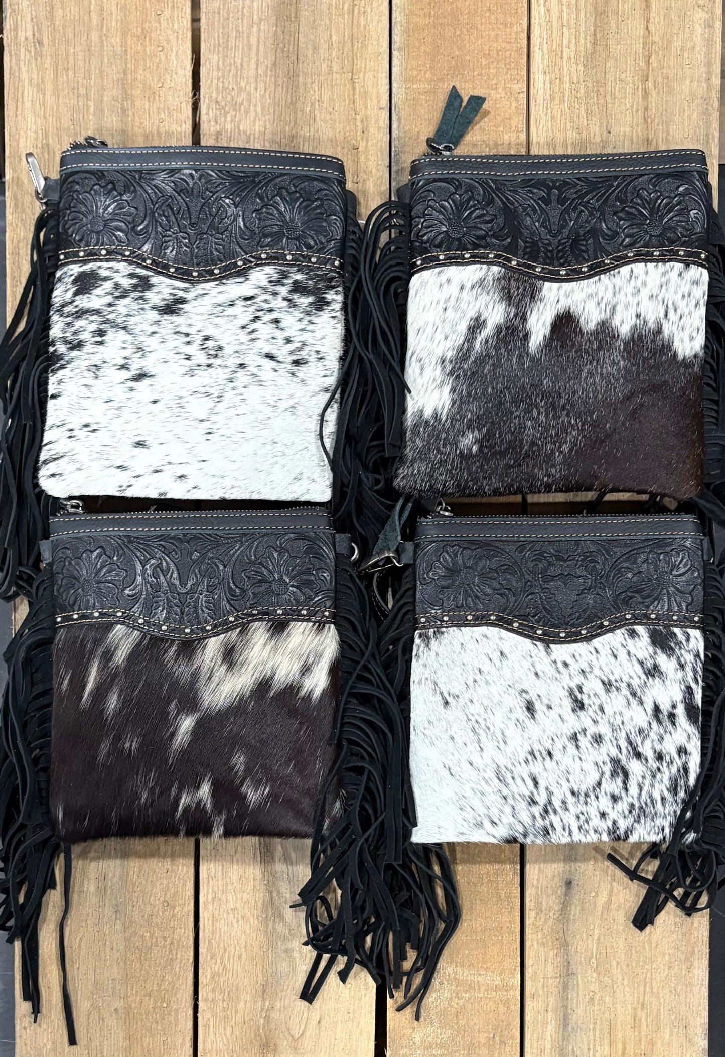 Four black and white cowhide handbags with fringe on a wooden surface
