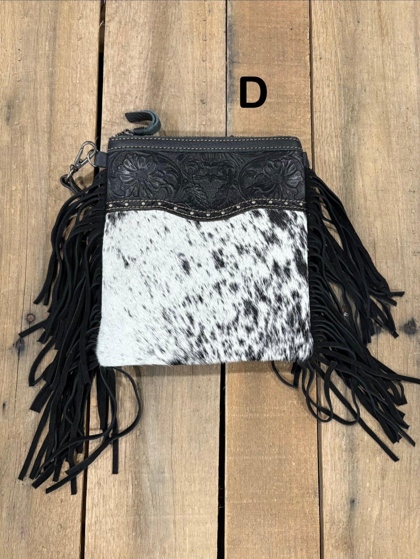 Black and white cowhide leather crossbody bag with fringe on a wooden surface