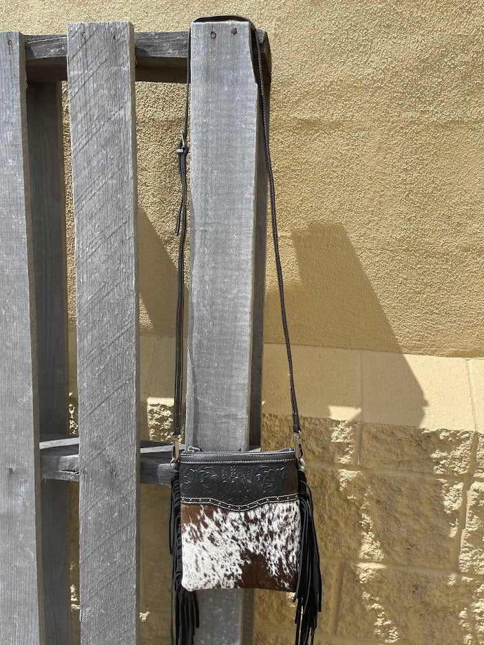 Black and white patterned crossbody bag with fringes hanging on a wooden ladder against a beige wall.