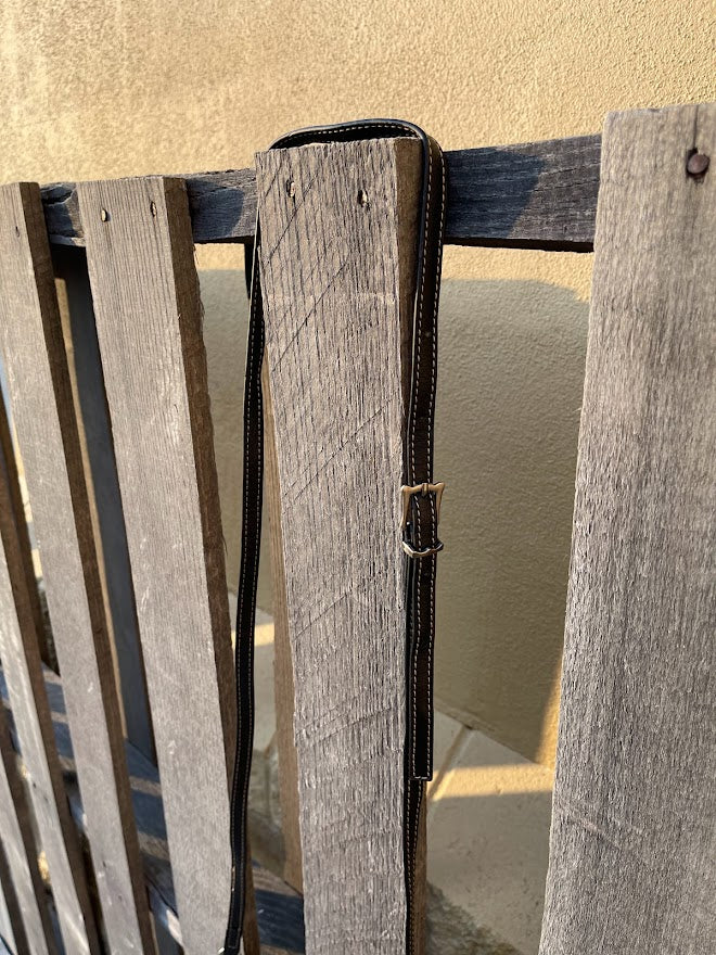 Black leather strap over a wooden chair with a beige wall in the background
