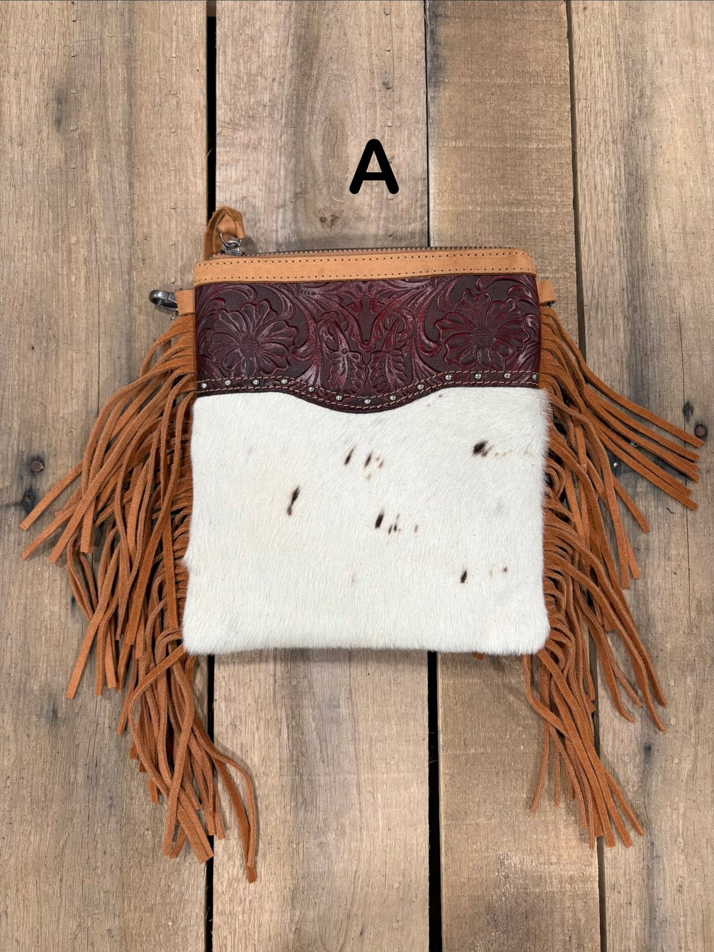 Brown handbag with hairon cowhide and leather accents and fringes on a wooden surface