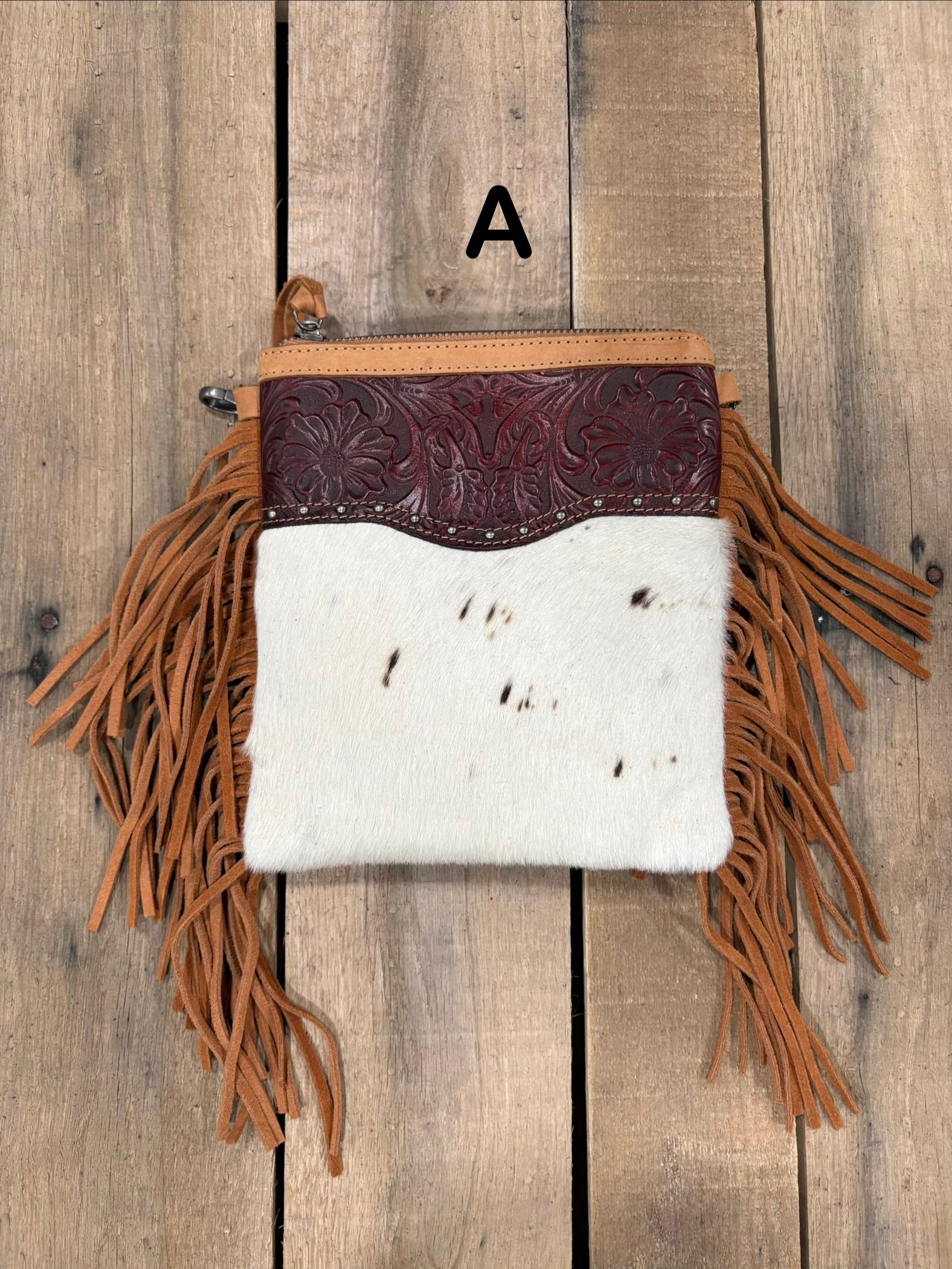 Brown handbag with hairon cowhide and leather accents and fringes on a wooden surface