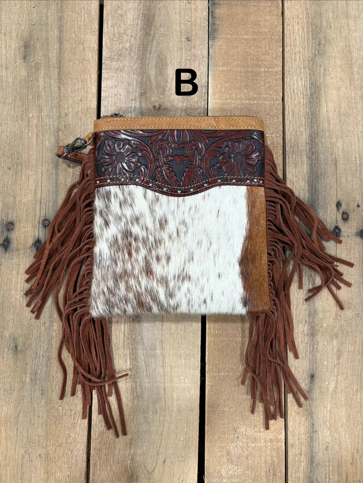 Brown handbag with hairon cowhide and leather accents and fringes on a wooden surface