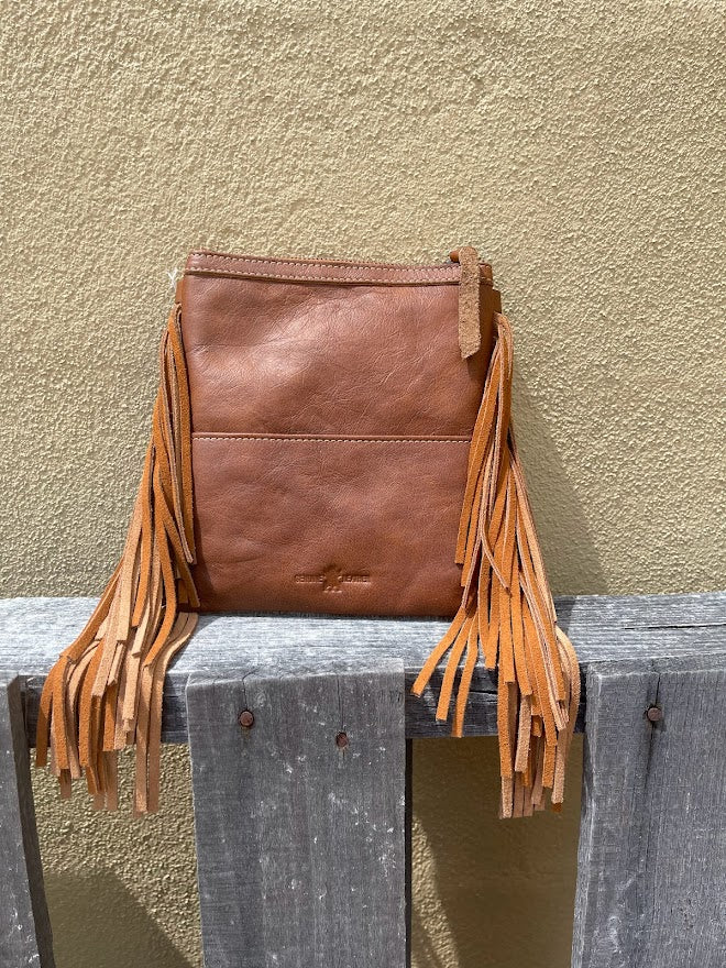 Brown leather bag with fringes on a wooden surface against a beige wall