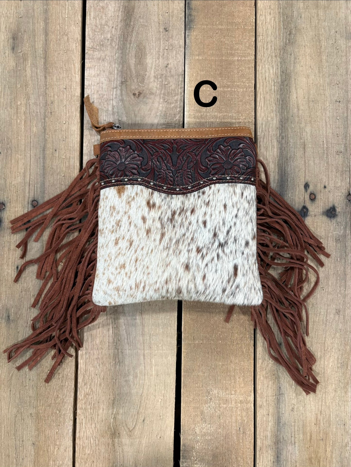 Brown handbag with hairon cowhide and leather accents and fringes on a wooden surface