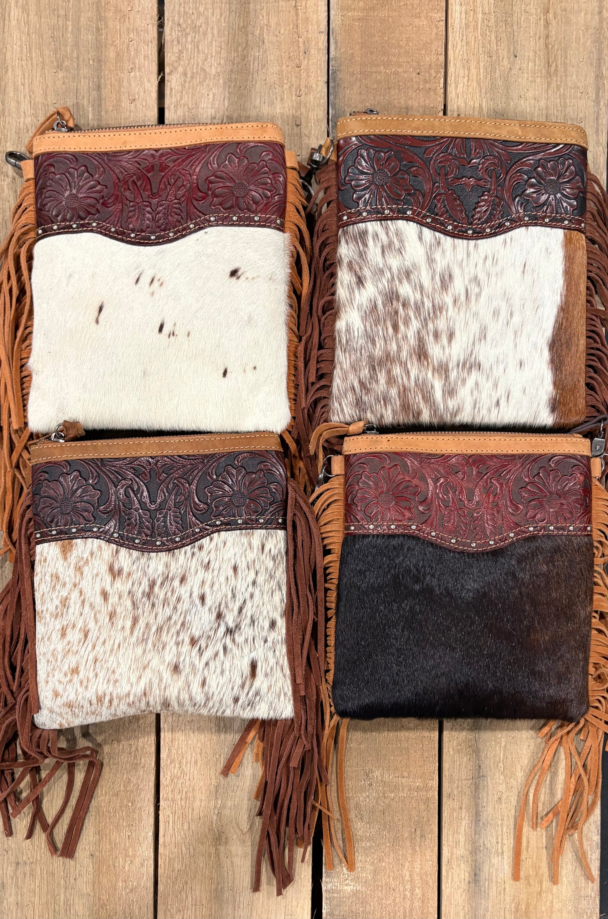 Four cowhide bags with leather accents and fringes on a wooden background