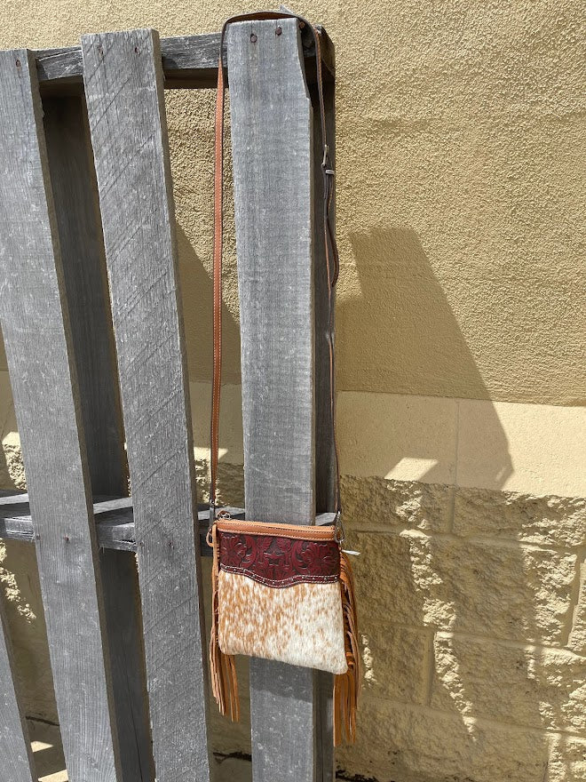 Handbag with a leather strap hanging on a wooden fence against a stone wall.