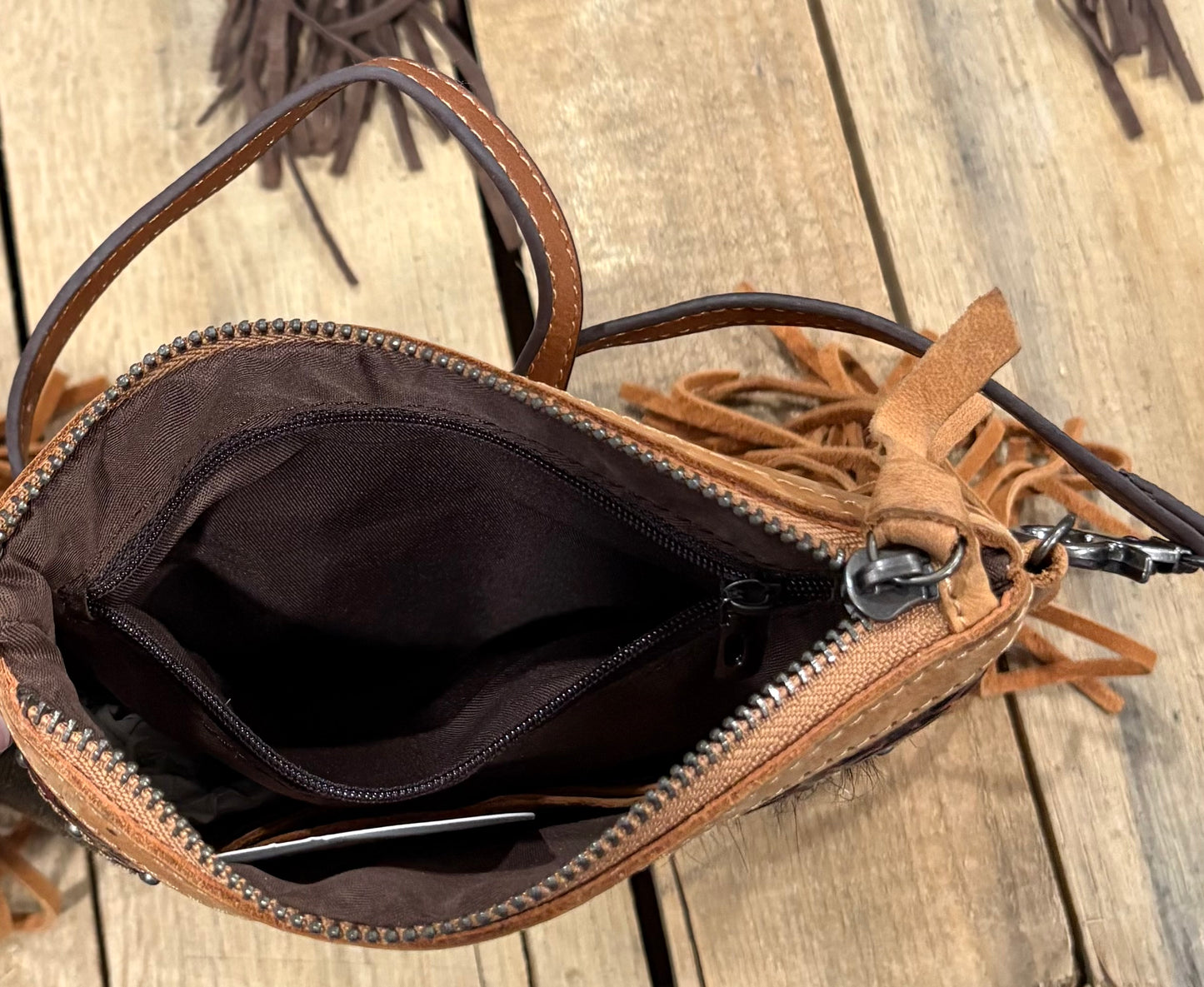 Inside zipper view of a Brown leather handbag with fringe details on a wooden surface