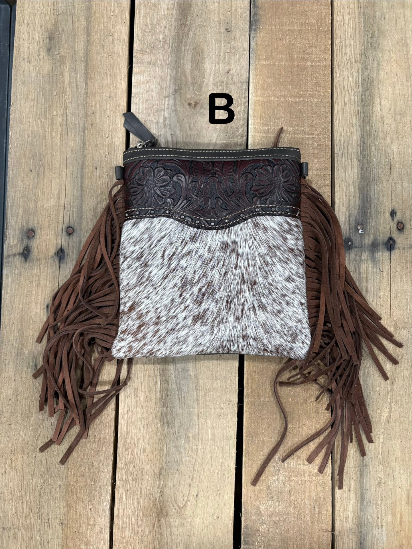 Coffee Brown handbag with hairon cowhide and leather accents and fringes on a wooden surface