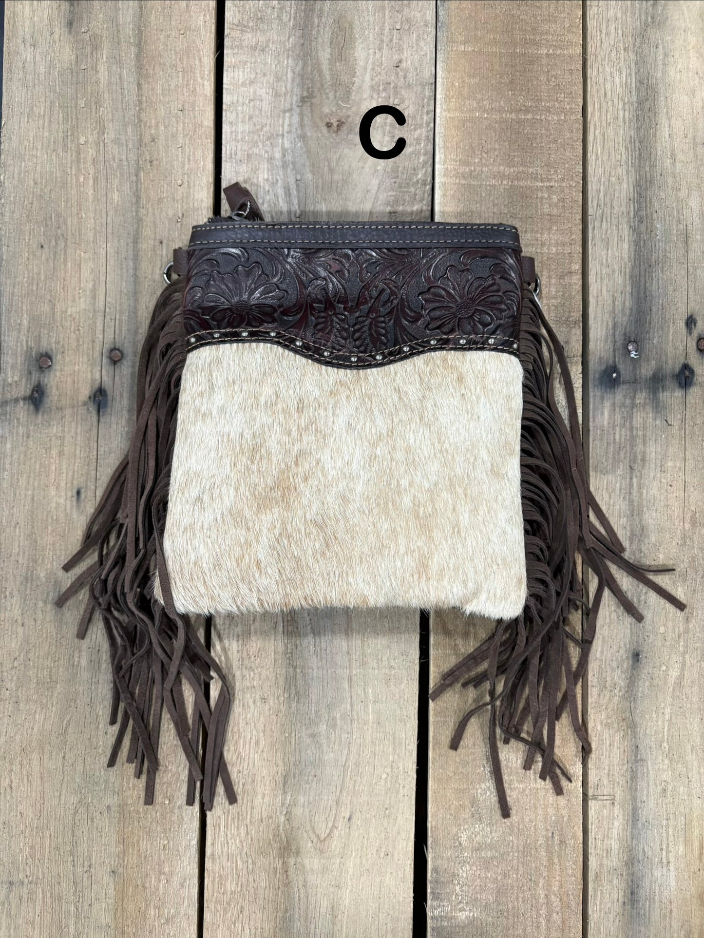 Coffee Brown handbag with hairon cowhide and leather accents and fringes on a wooden surface