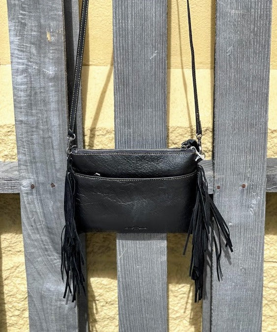 Back view of a small crossbody bag with turquoise and black cowhide and fringe hanging against a wooden background.