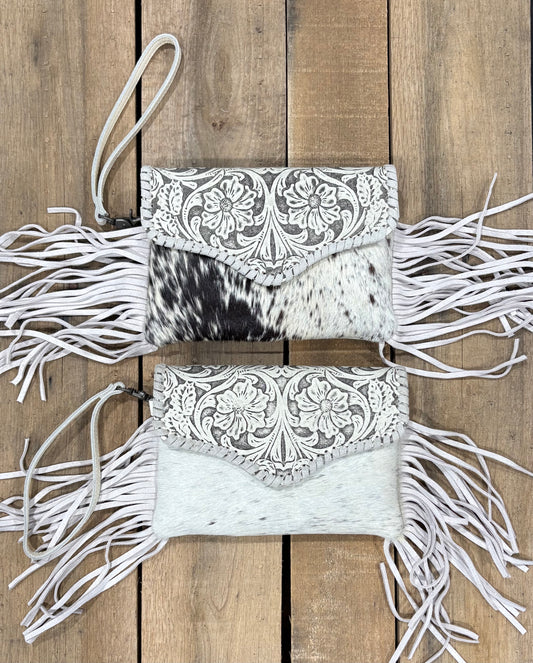 Two white handbags with black and white cowhide pattern and white fringe on a wooden background
