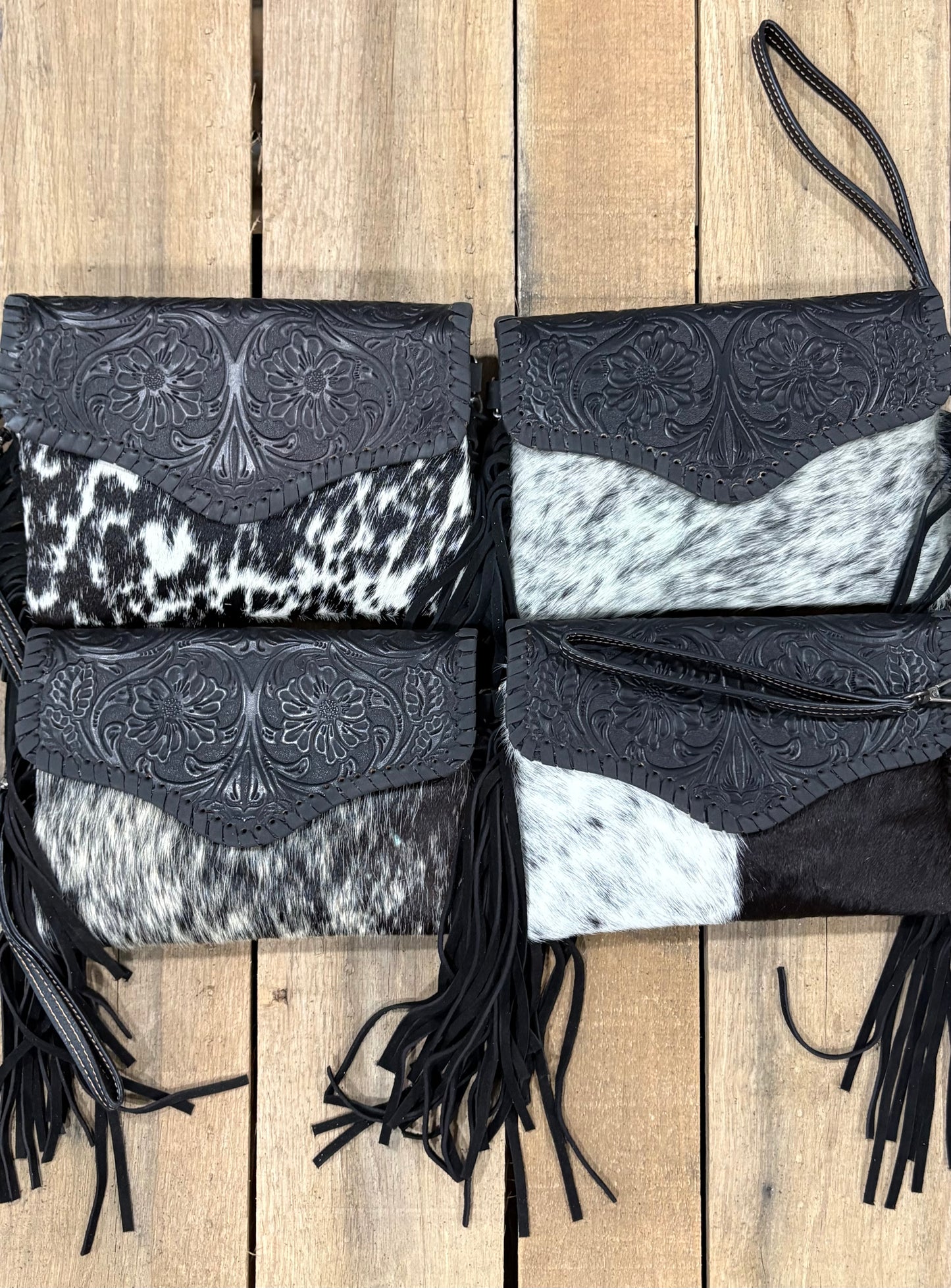Four cowhide handbags with black fringe on a wooden surface