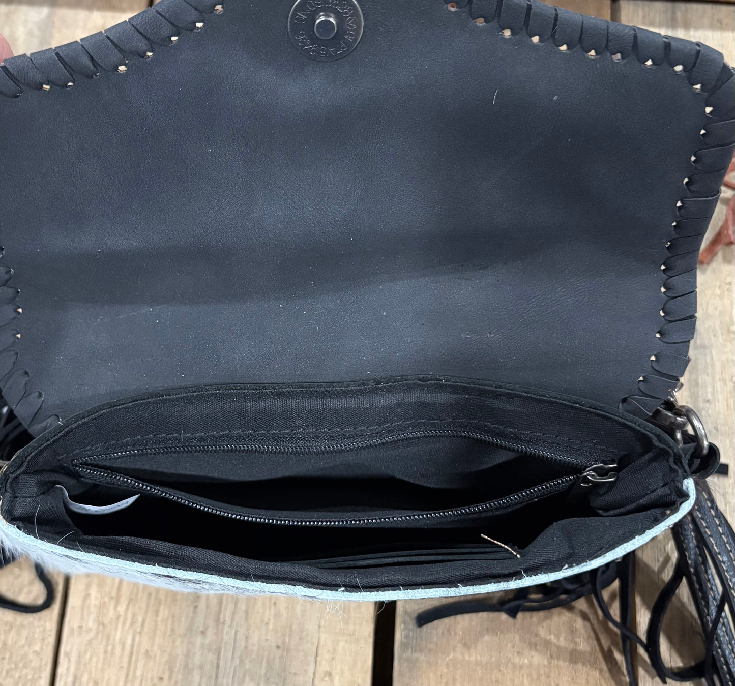 Inside zipper view of a Black handbag with fringe details on a wooden surface